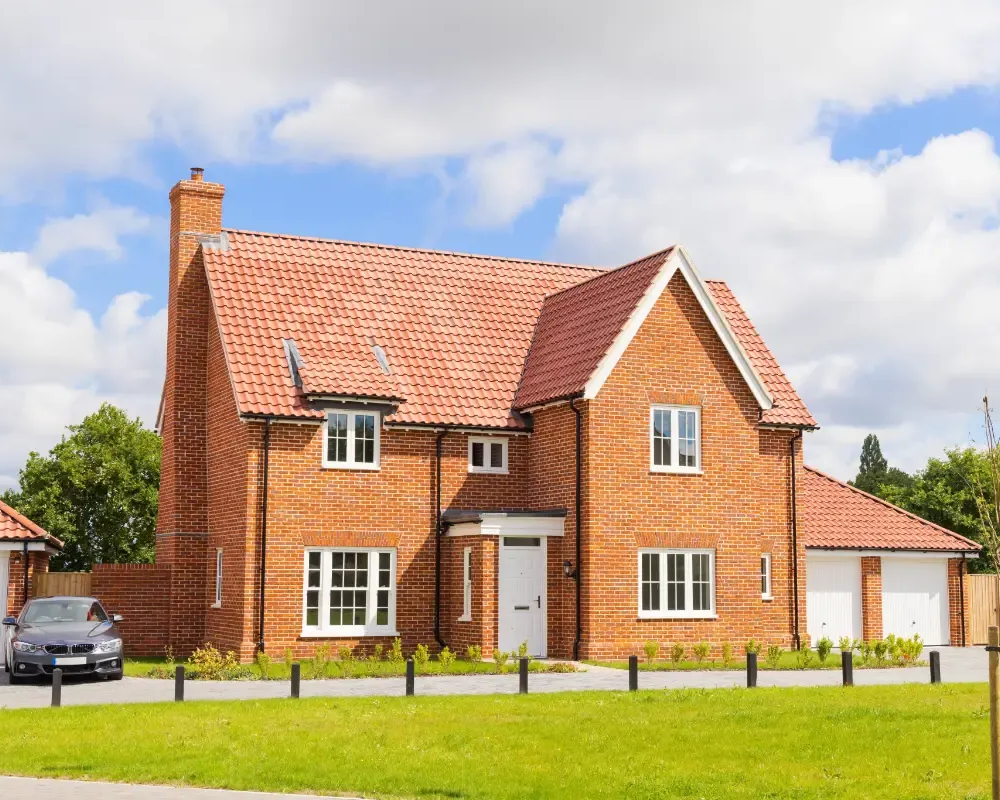 Core One Construction | Brick house with red roof and white trim, two-car garage, green lawn, and car parked in front.