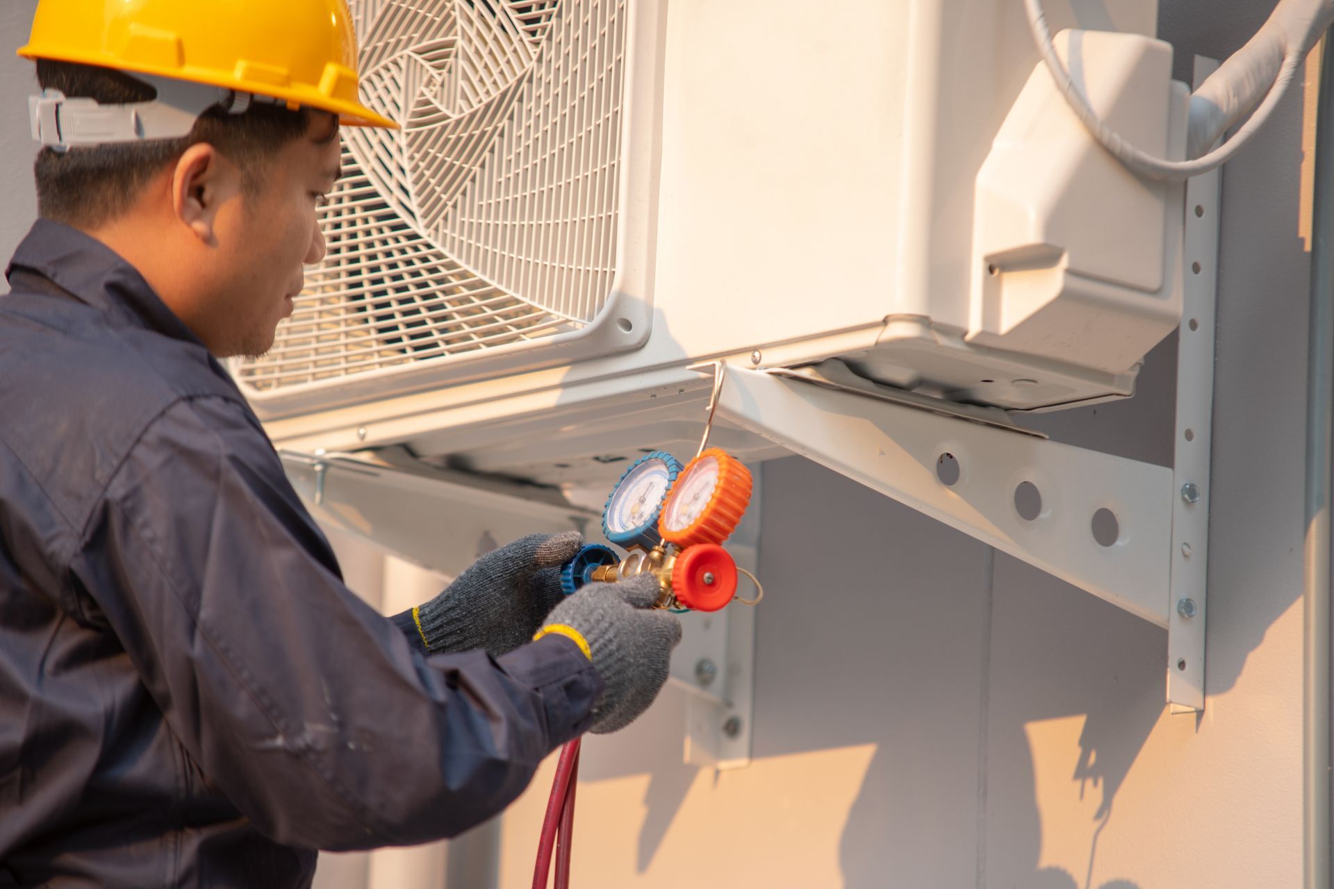 Technician in hard hat testing an outdoor air conditioner unit with a multimeter