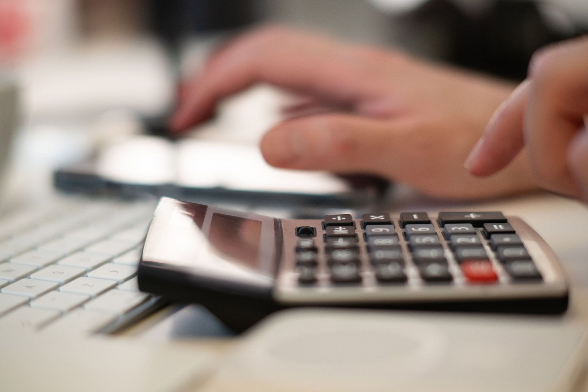 Calculator on a desk with a hand typing on a keyboard in the background