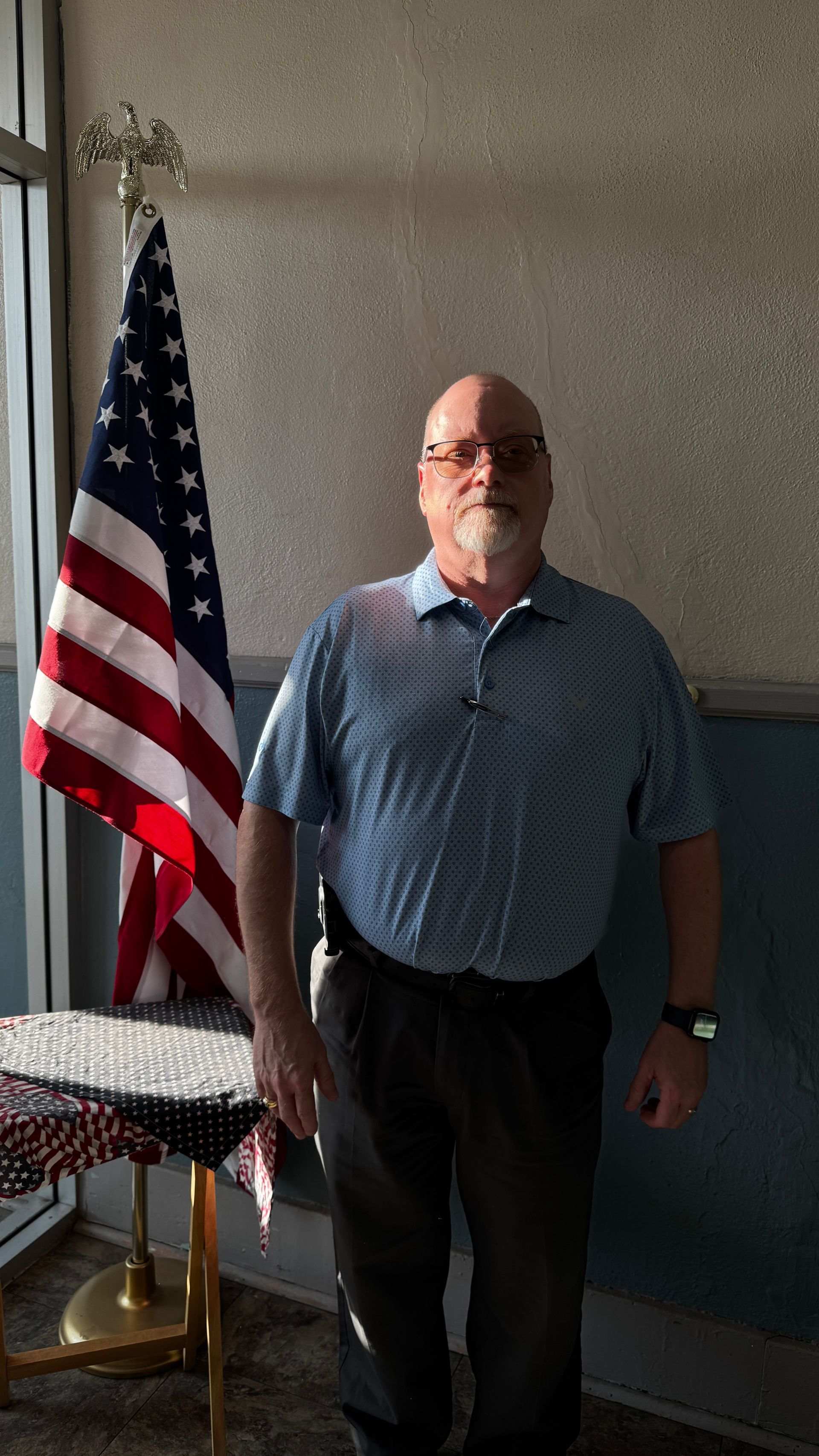 Man standing next to an American flag, in front of a textured wall.