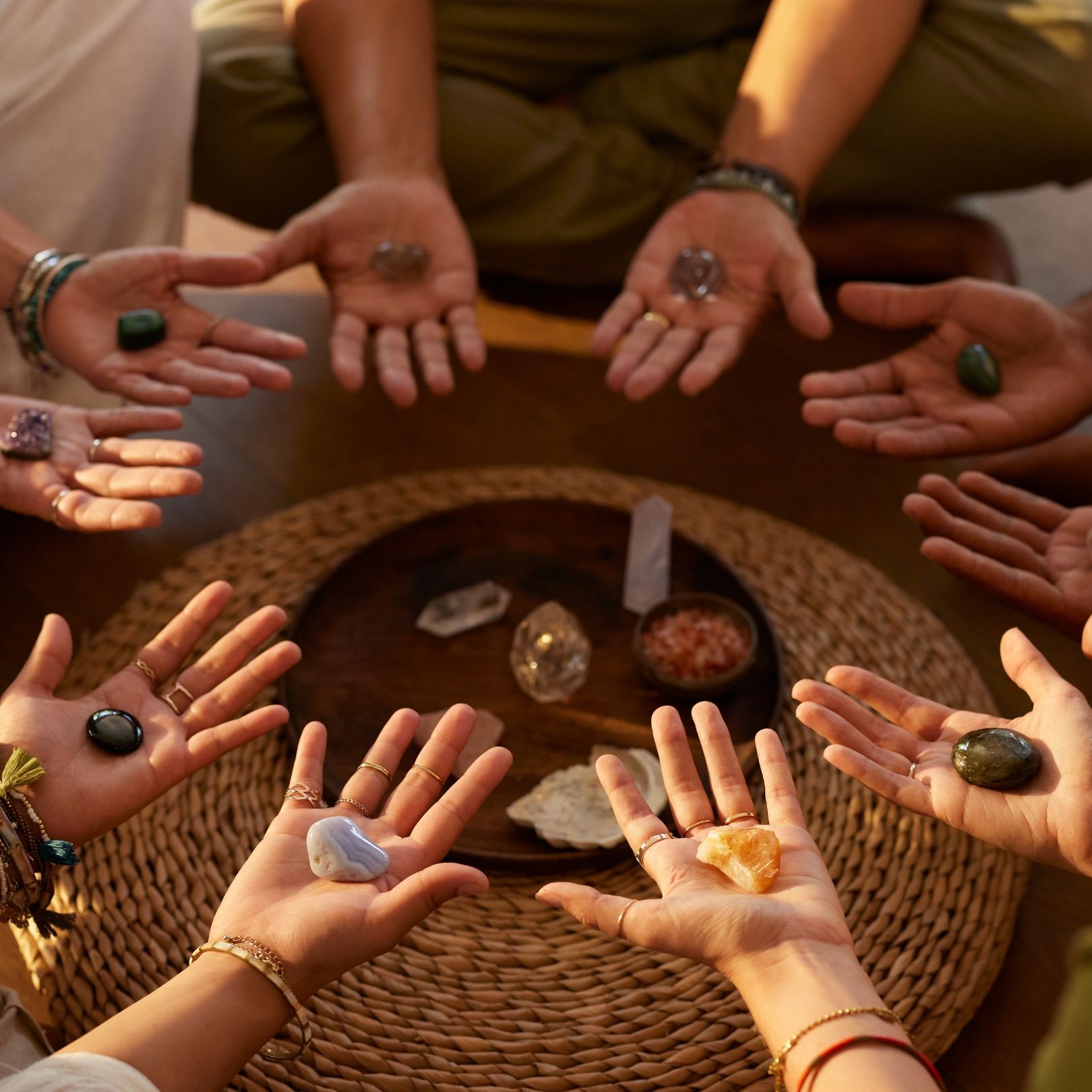 A group of people sitting in a circle, each holding a different healing crystal in their open palms over a central tray.