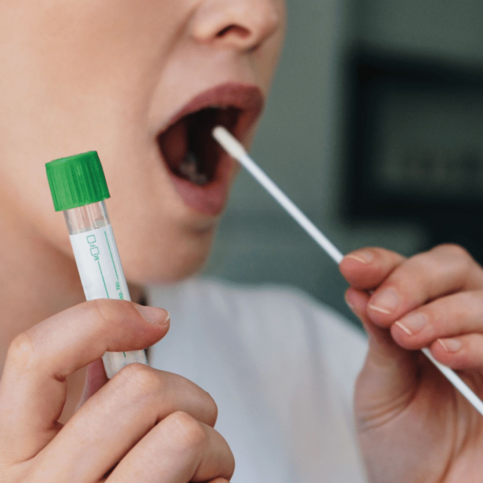 A close-up of a person performing a medical throat swab test, holding a specimen tube with a green cap.