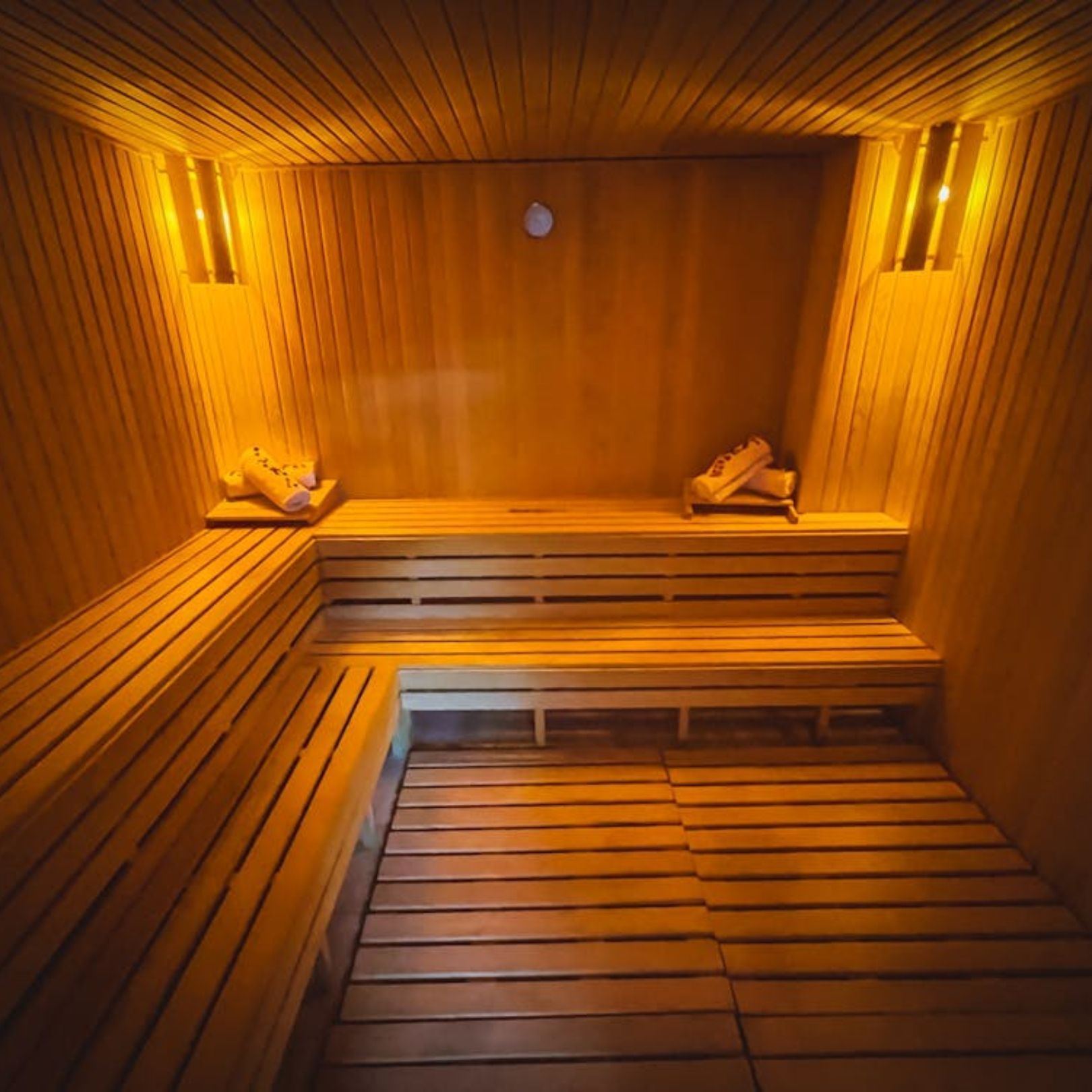A warm-toned wooden sauna interior featuring tiered benches, slatted flooring, and soft wall lighting.