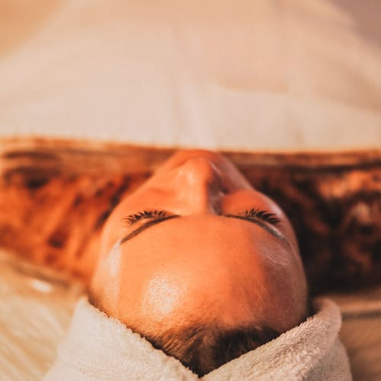 A person lying on their back with a white headband, eyes closed, during a relaxing spa or facial treatment.