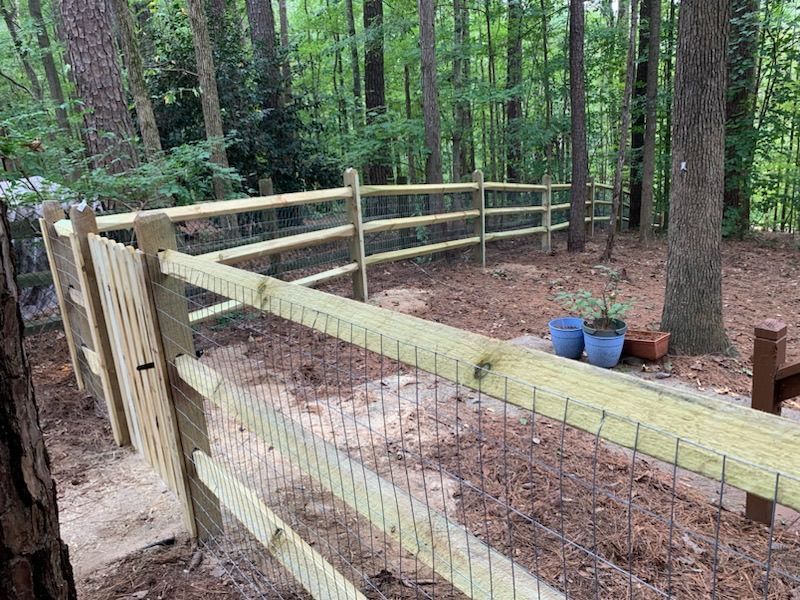 A wooden fence with a wire fence in the middle of a forest.