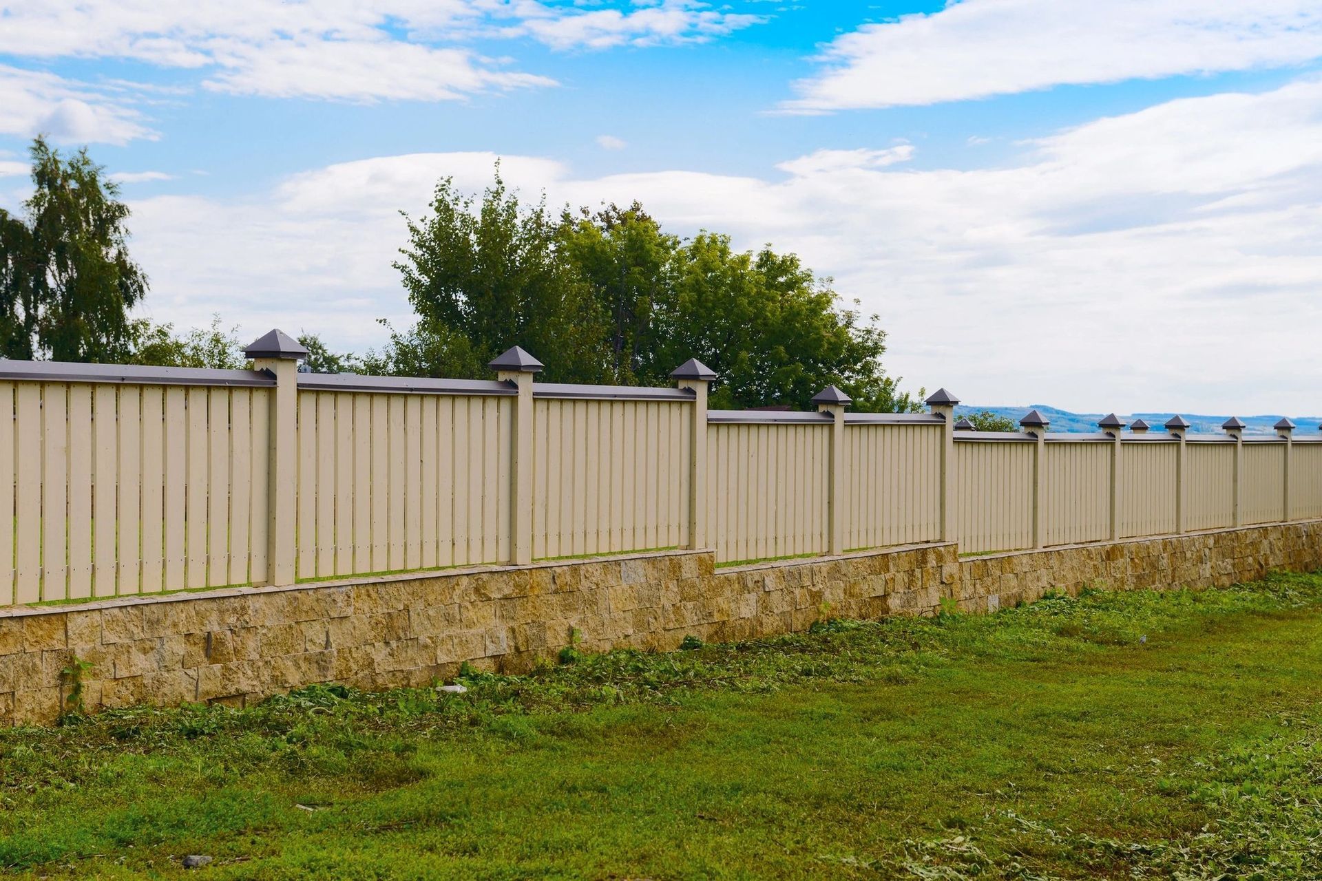 A wooden fence surrounds a grassy field with trees in the background.