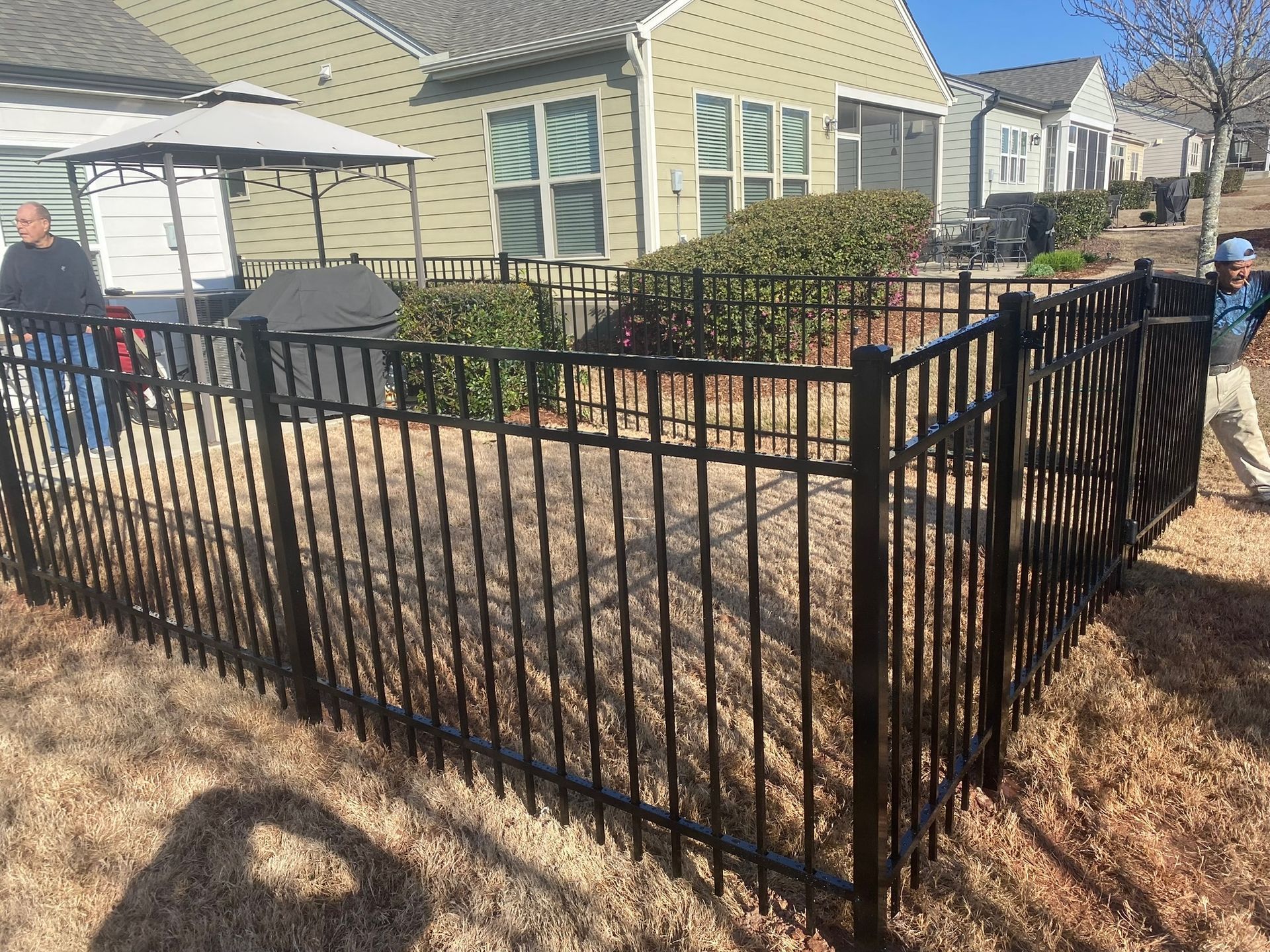 A man is standing next to a black fence in front of a house.
