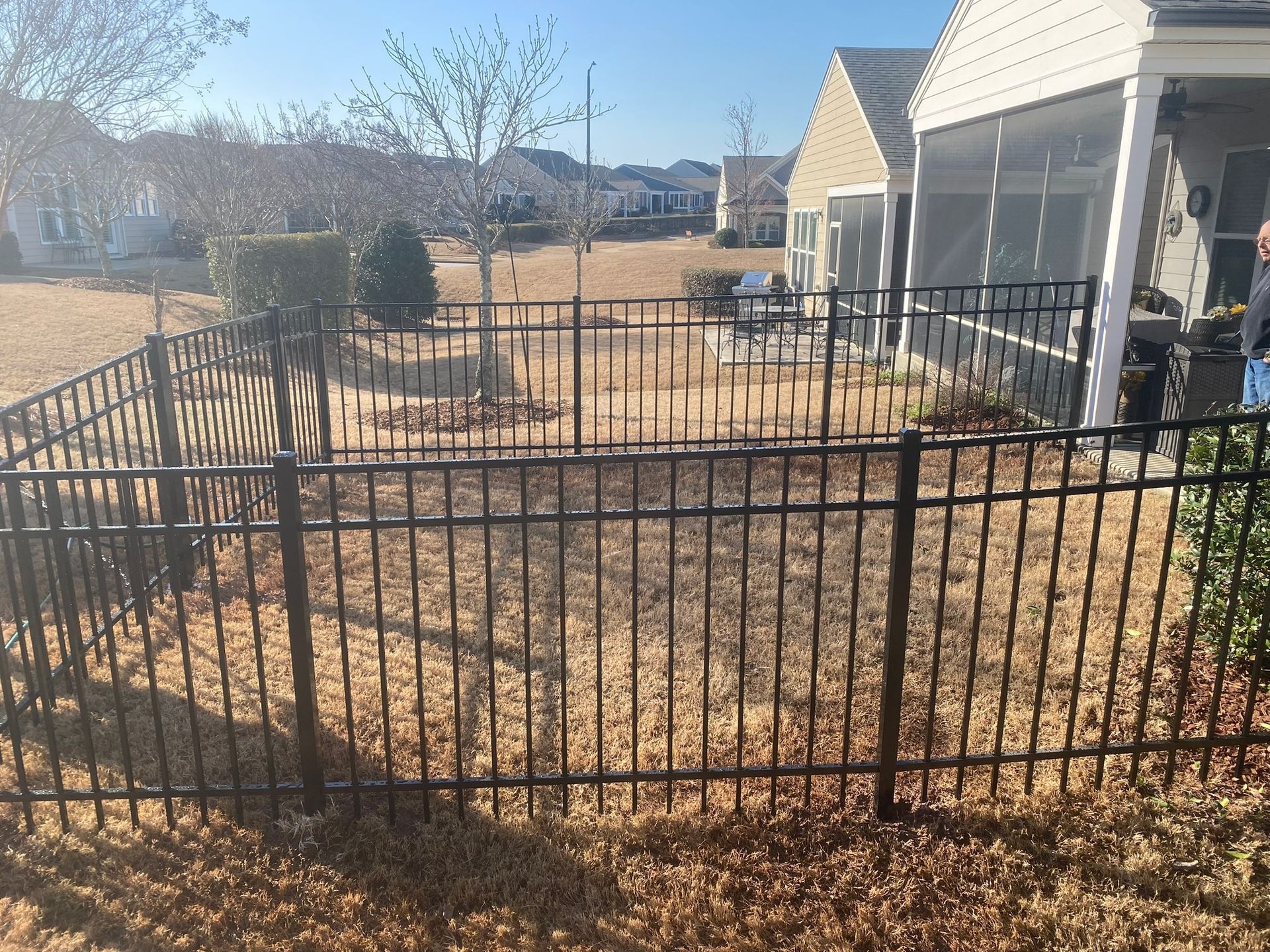 A black metal fence surrounds a yard in front of a house.