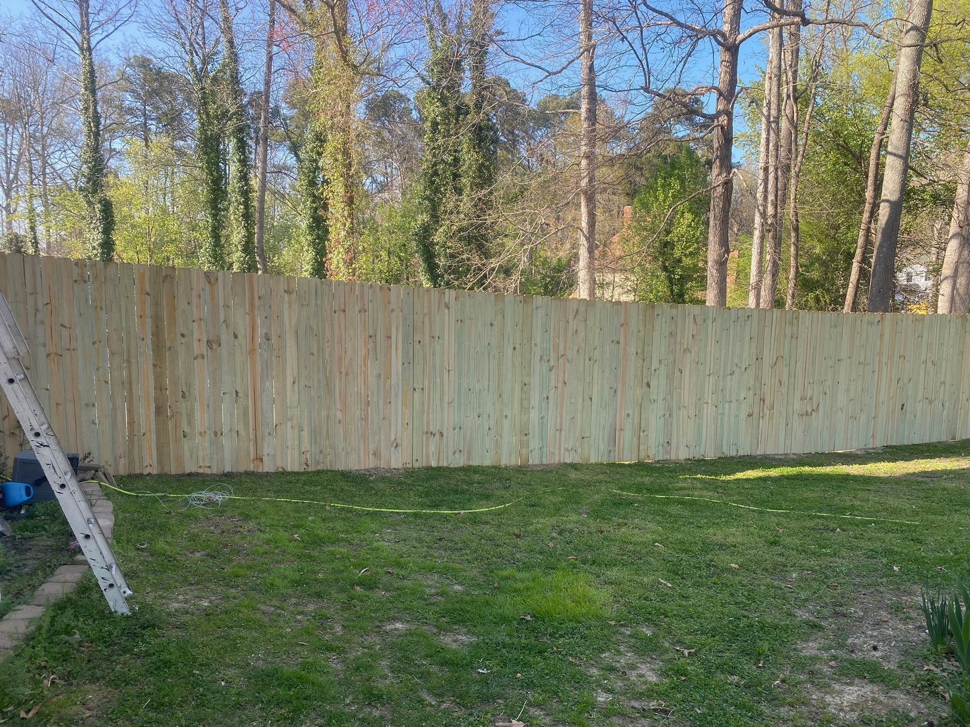 A wooden fence is being built in a backyard with trees in the background.