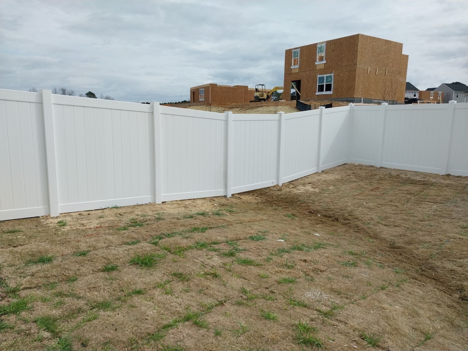 A white fence surrounds a yard with a house in the background.
