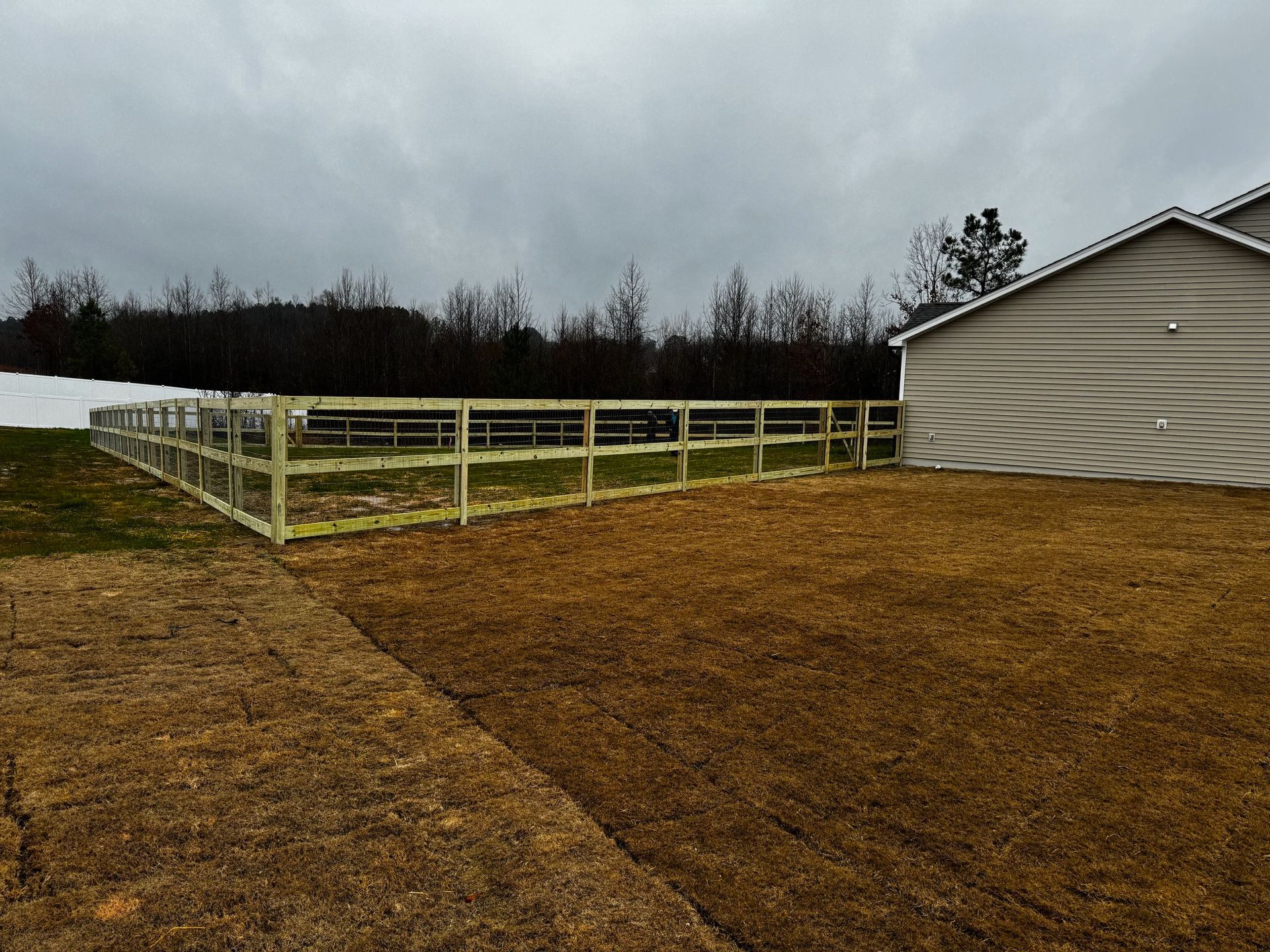 A wooden fence surrounds a dirt field in front of a house.