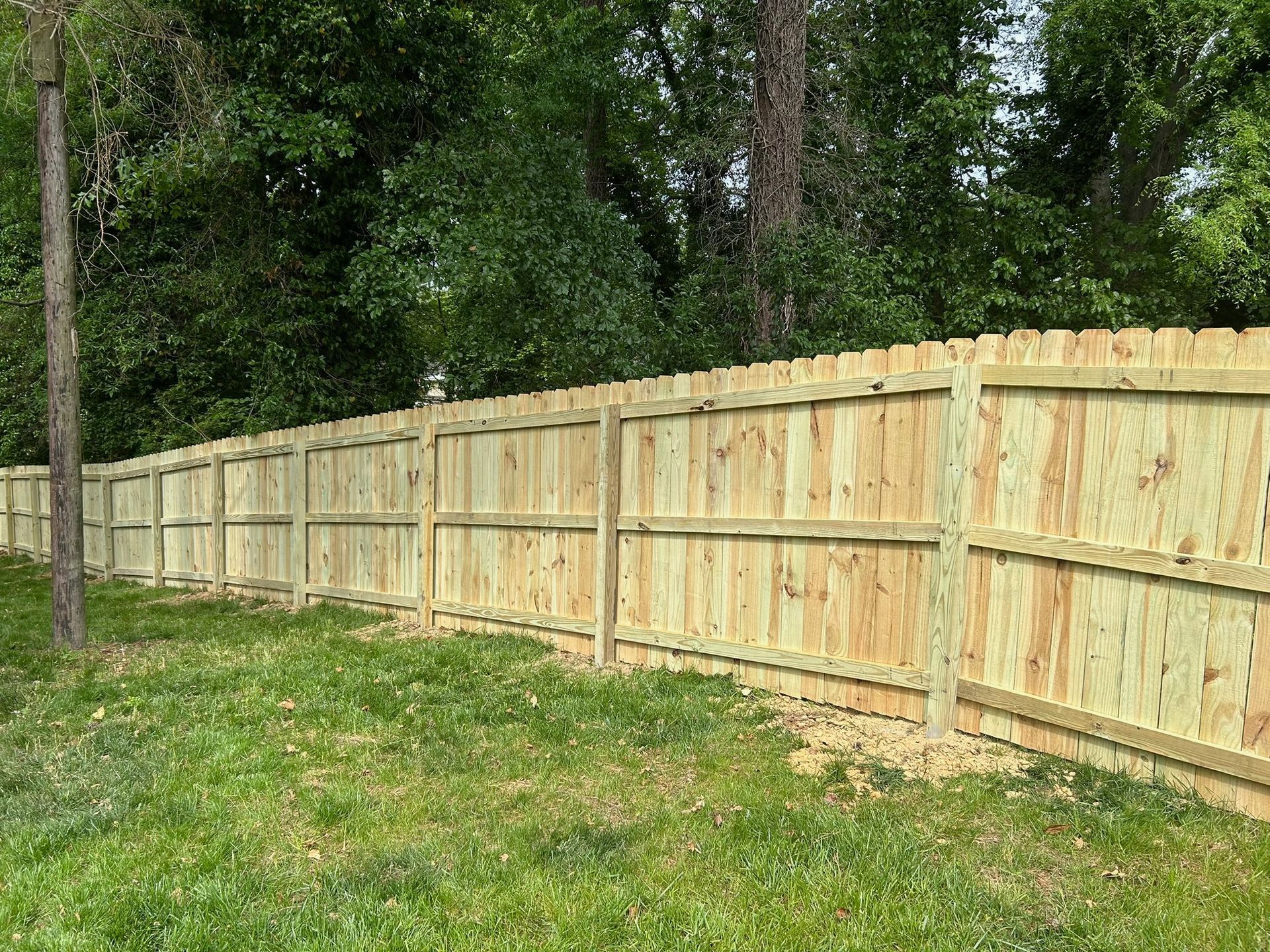 A wooden fence is surrounded by trees and grass in a yard.
