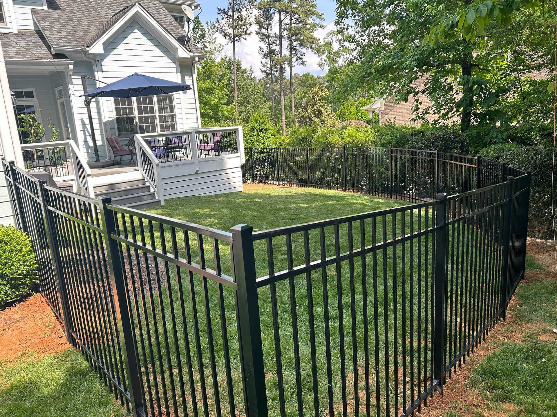 A black fence surrounds a lush green yard in front of a house.