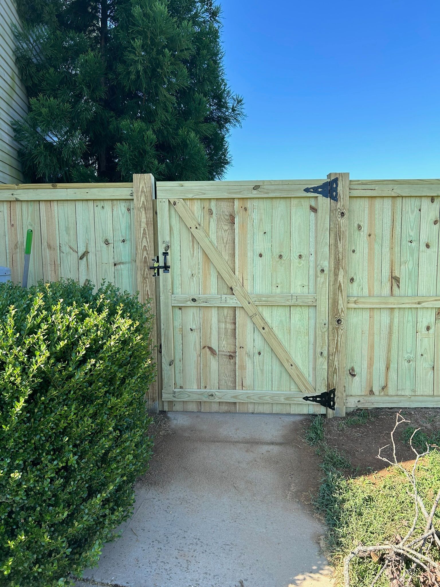 A wooden fence with a gate leading to a concrete walkway.