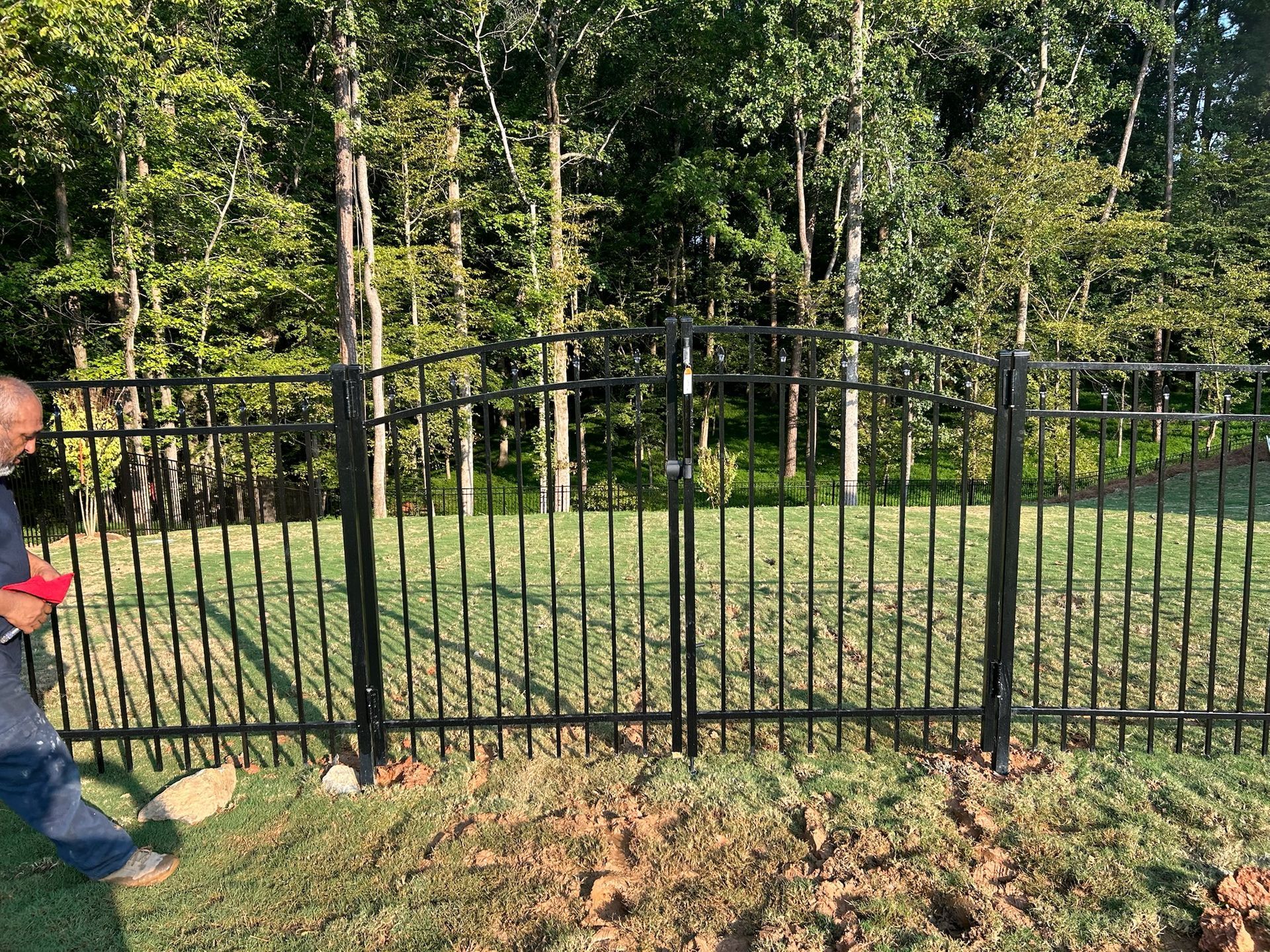 A man is standing in front of a wrought iron fence in a yard.