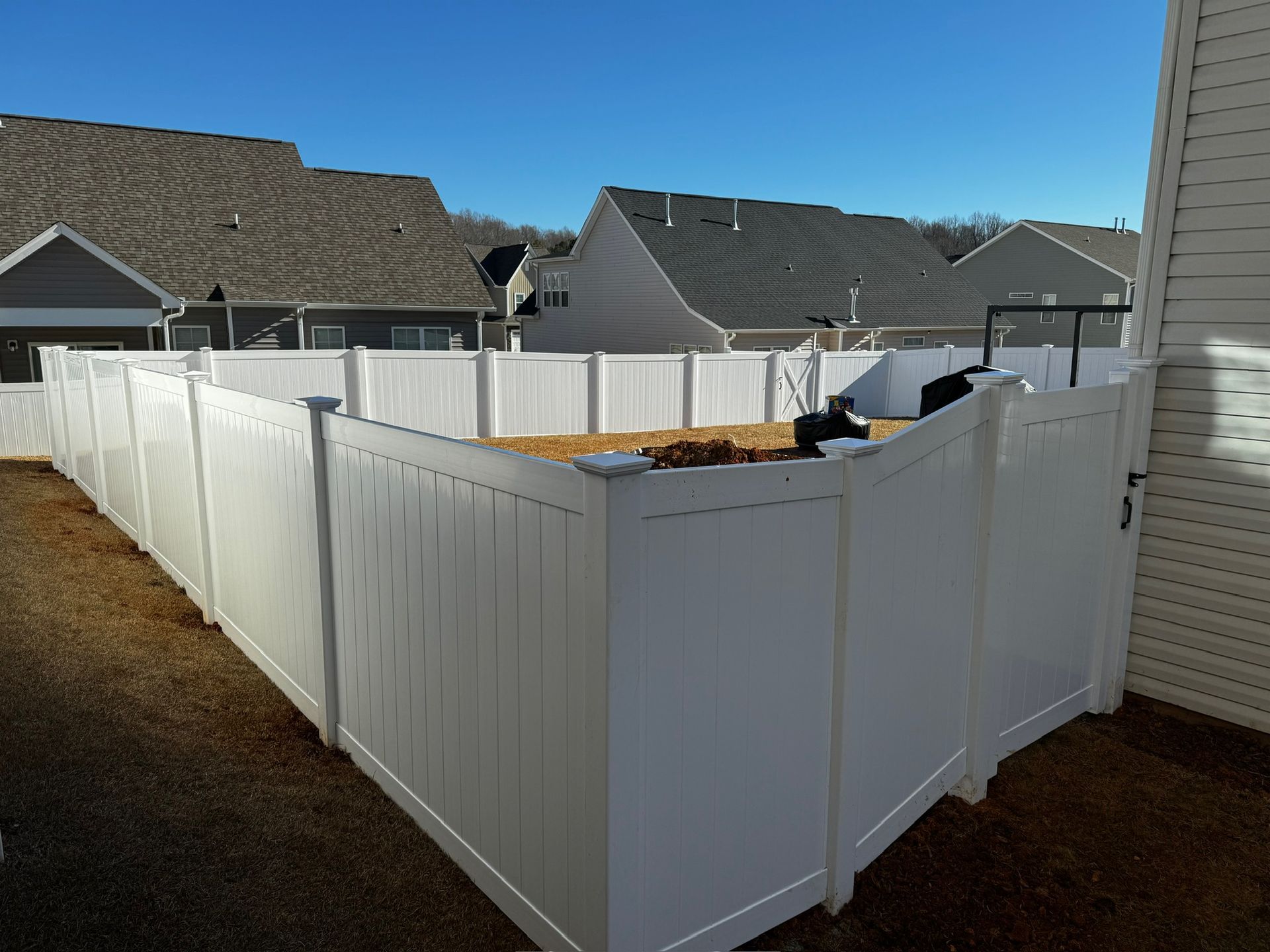 A white fence surrounds a yard with houses in the background.