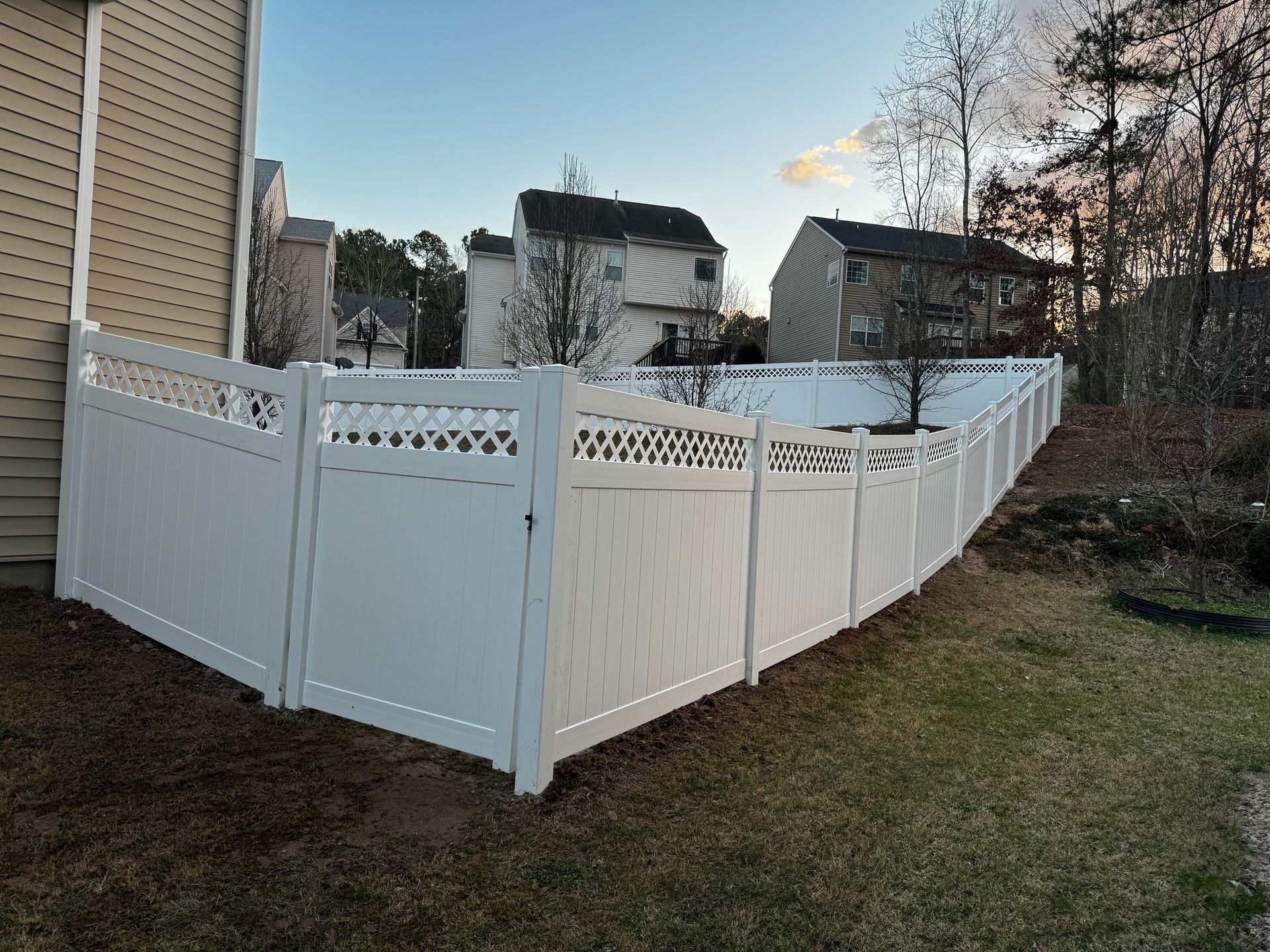 A white fence is in the backyard of a house.