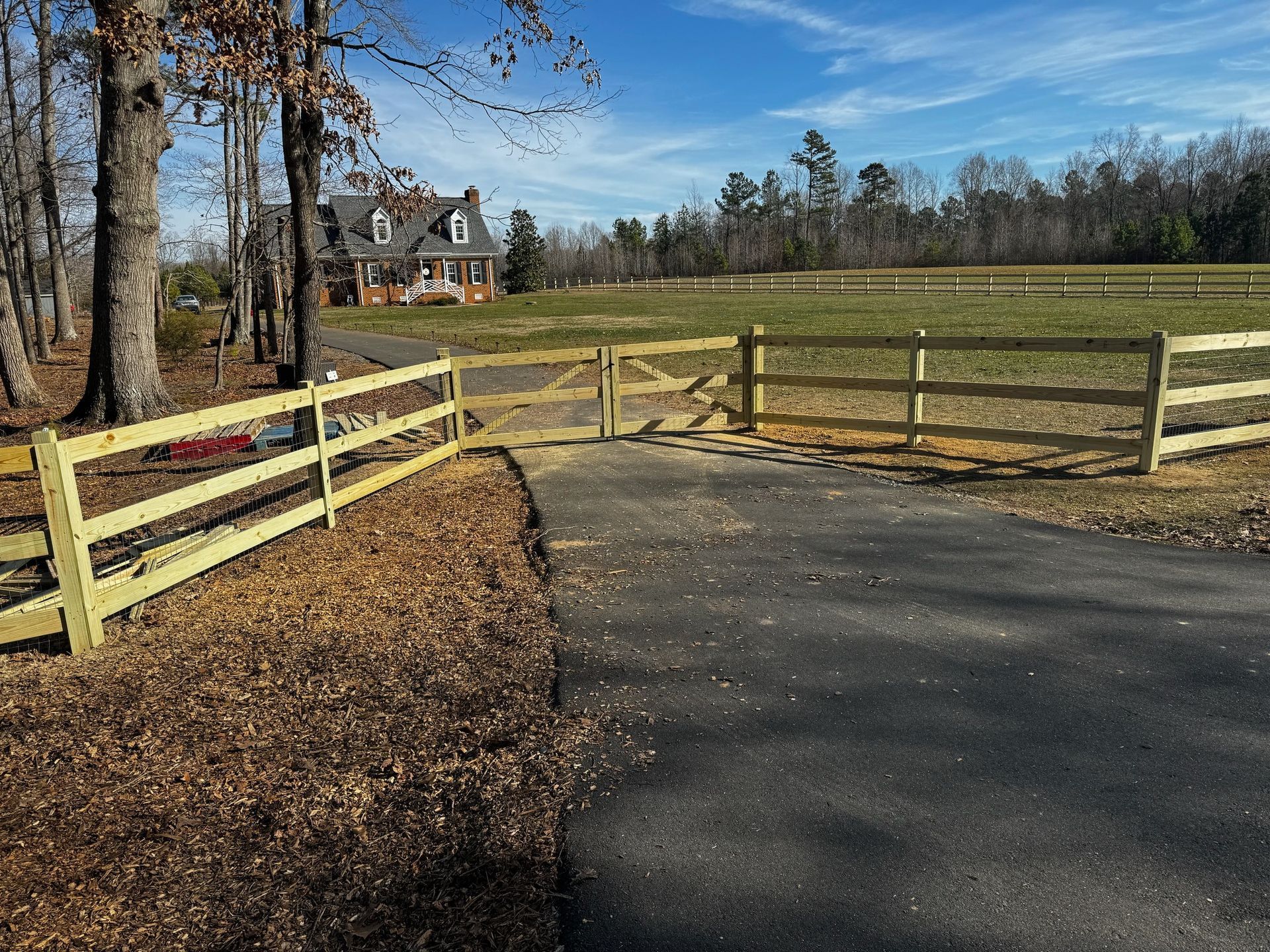 A wooden fence surrounds a driveway leading to a house.