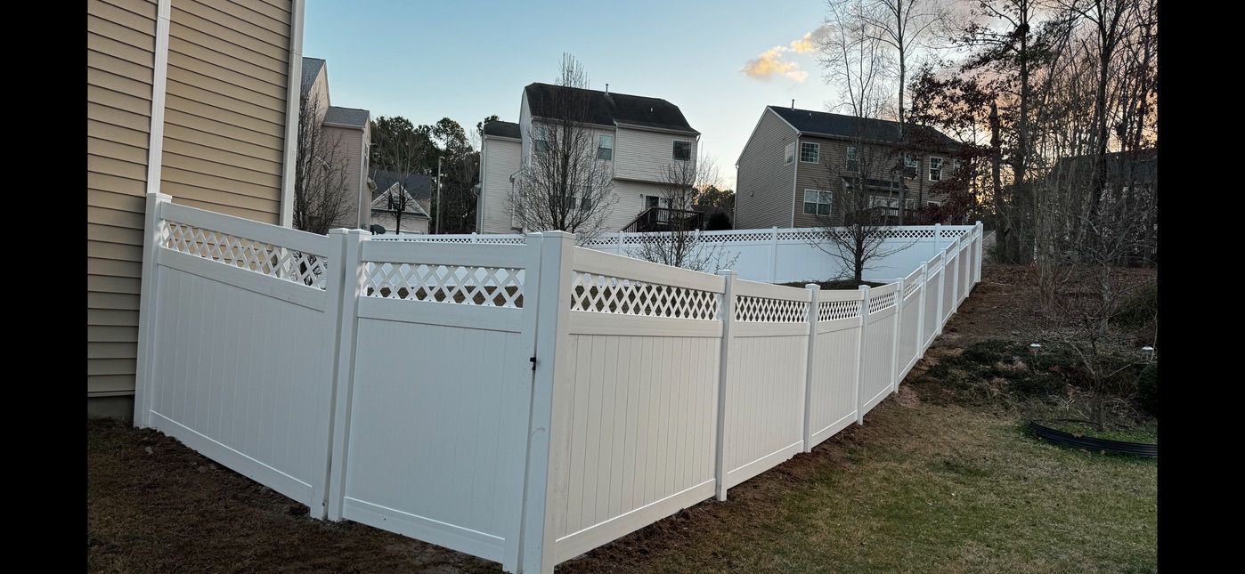 A white fence is surrounding a backyard with houses in the background.