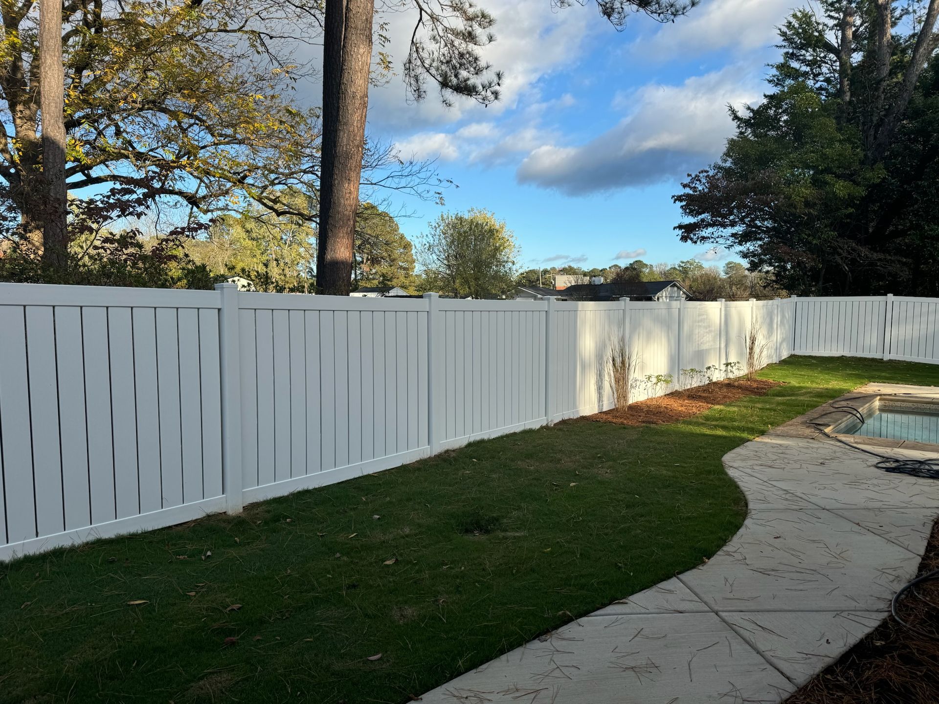 A white fence surrounds a swimming pool in a backyard.