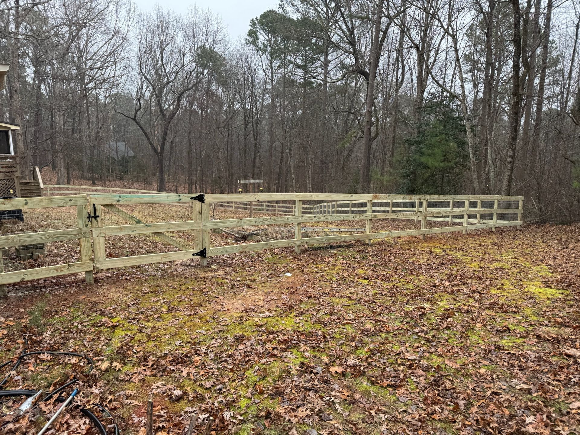 A wooden fence is in the middle of a field surrounded by trees.