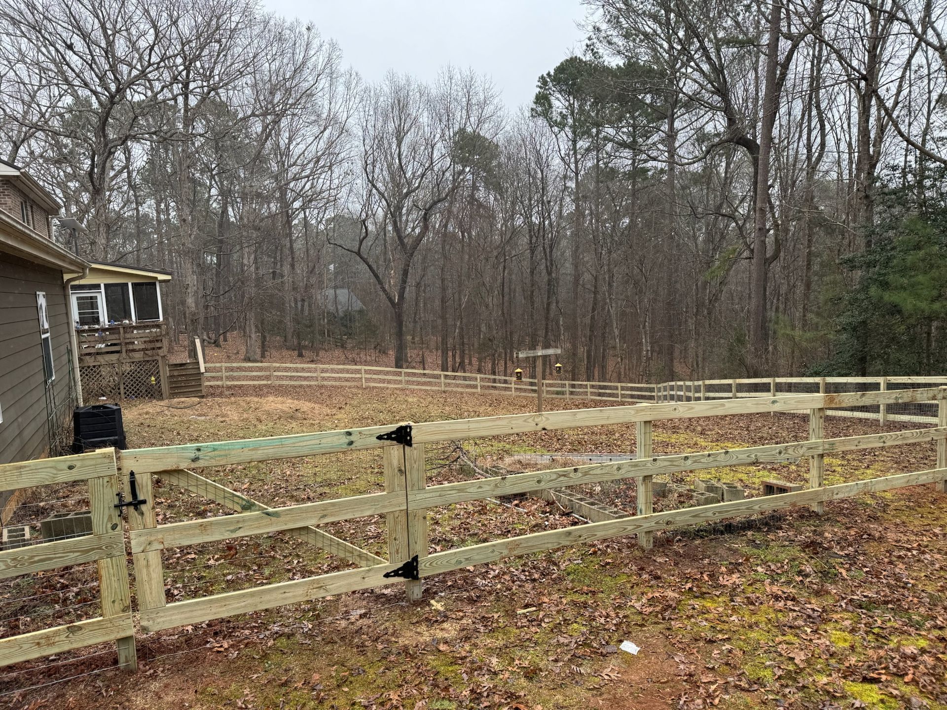 A wooden fence surrounds a field with trees in the background.