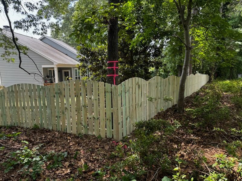 A wooden fence is surrounded by trees and bushes in front of a house.