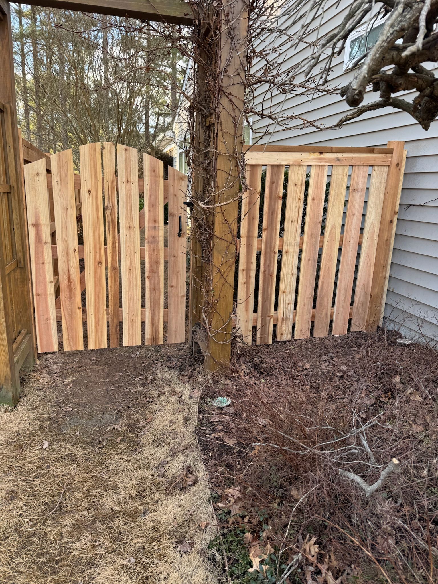A wooden fence is sitting next to a tree in front of a house.