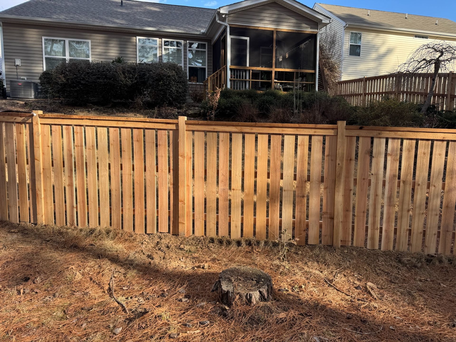 A wooden fence surrounds a house with a screened in porch.