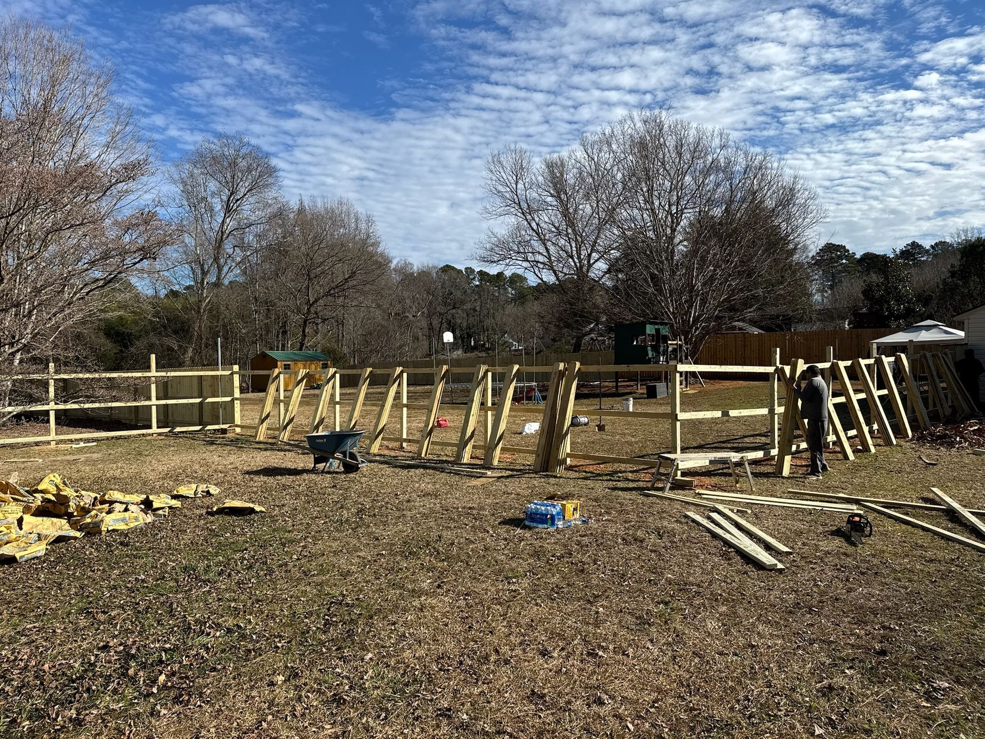 A wooden fence is being built in a field with trees in the background.