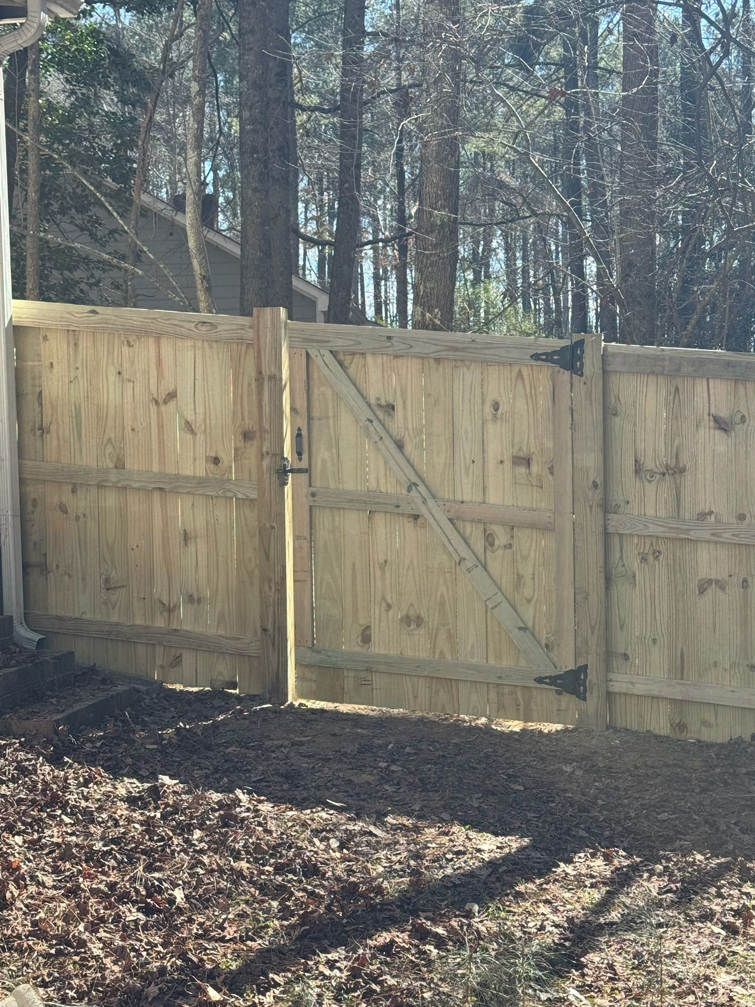 A wooden fence with a gate is surrounded by trees.
