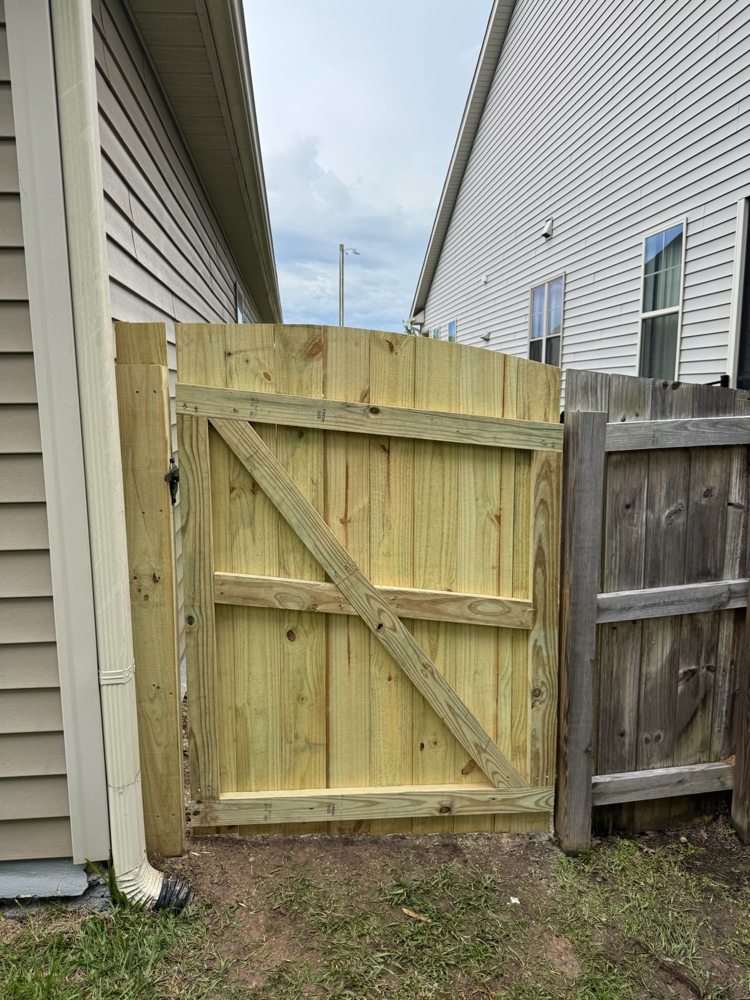 A wooden gate is sitting next to a wooden fence next to a house.