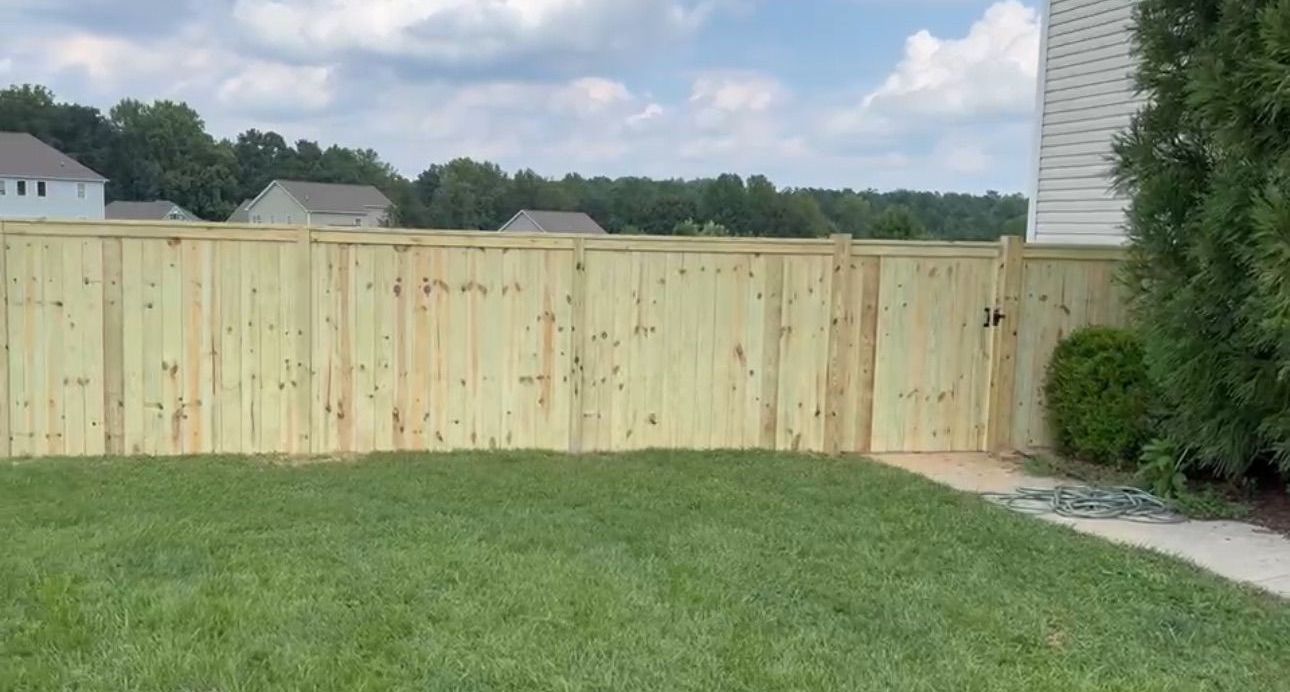 A wooden fence surrounds a lush green lawn in a backyard.