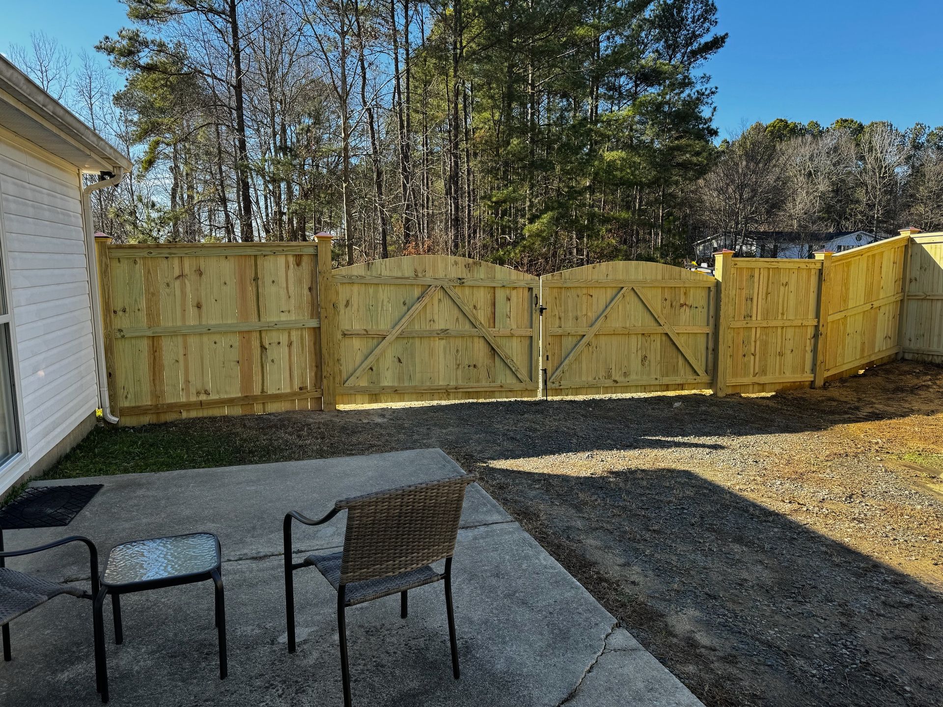 A wooden fence is surrounding a patio with chairs and a table.