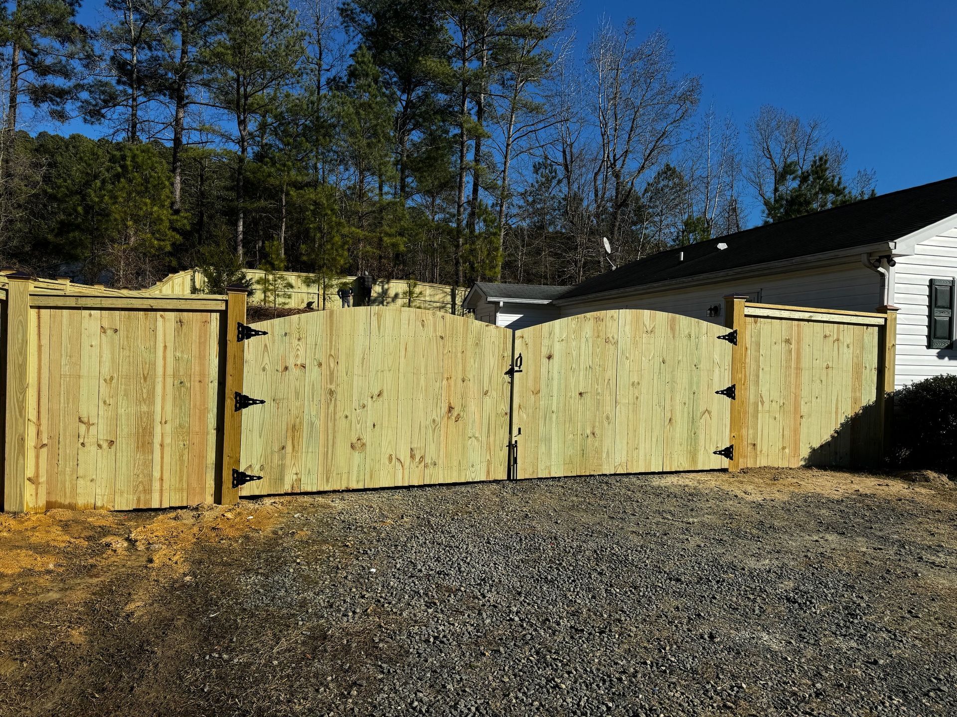 A wooden fence is surrounding a gravel driveway in front of a house.