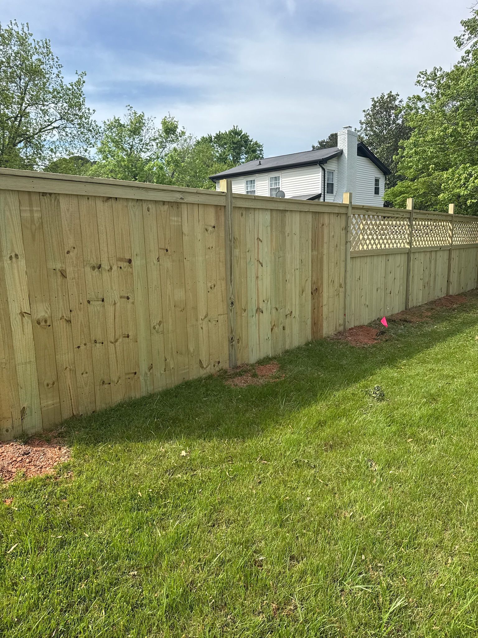 A wooden fence in a backyard with a house in the background.