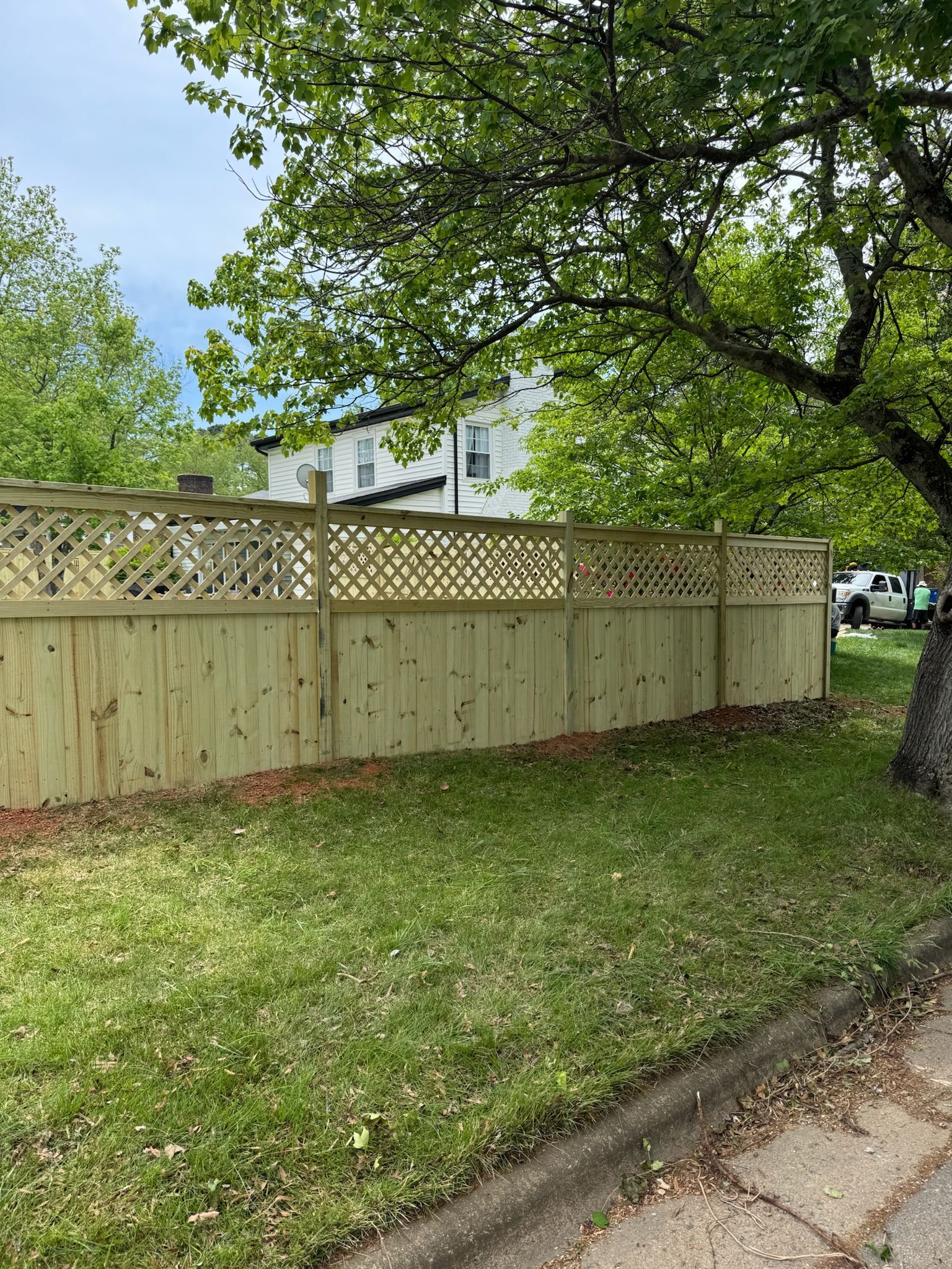 A wooden fence is surrounded by grass and trees in front of a house.