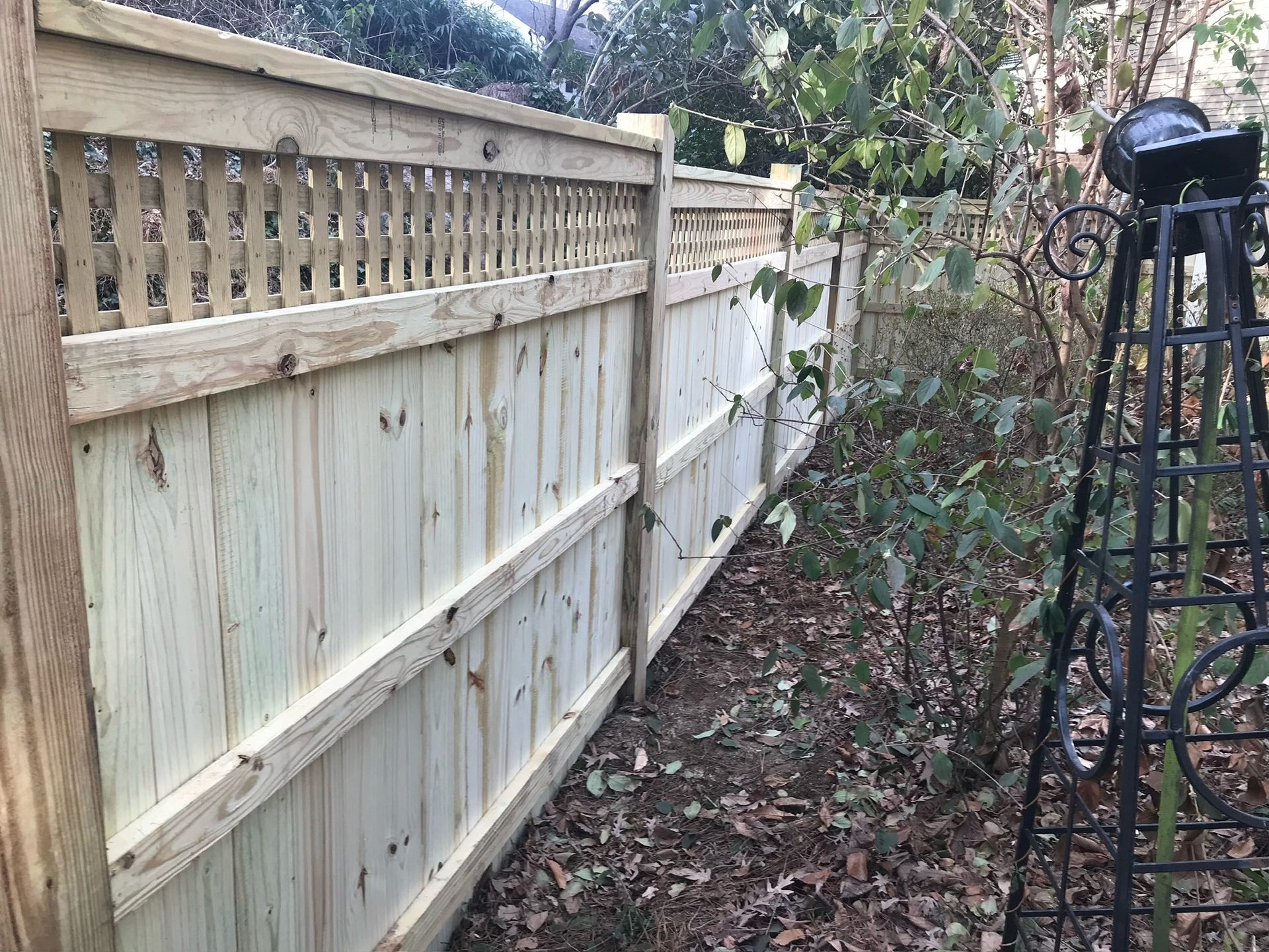 A wooden fence is surrounded by trees and leaves in a yard.