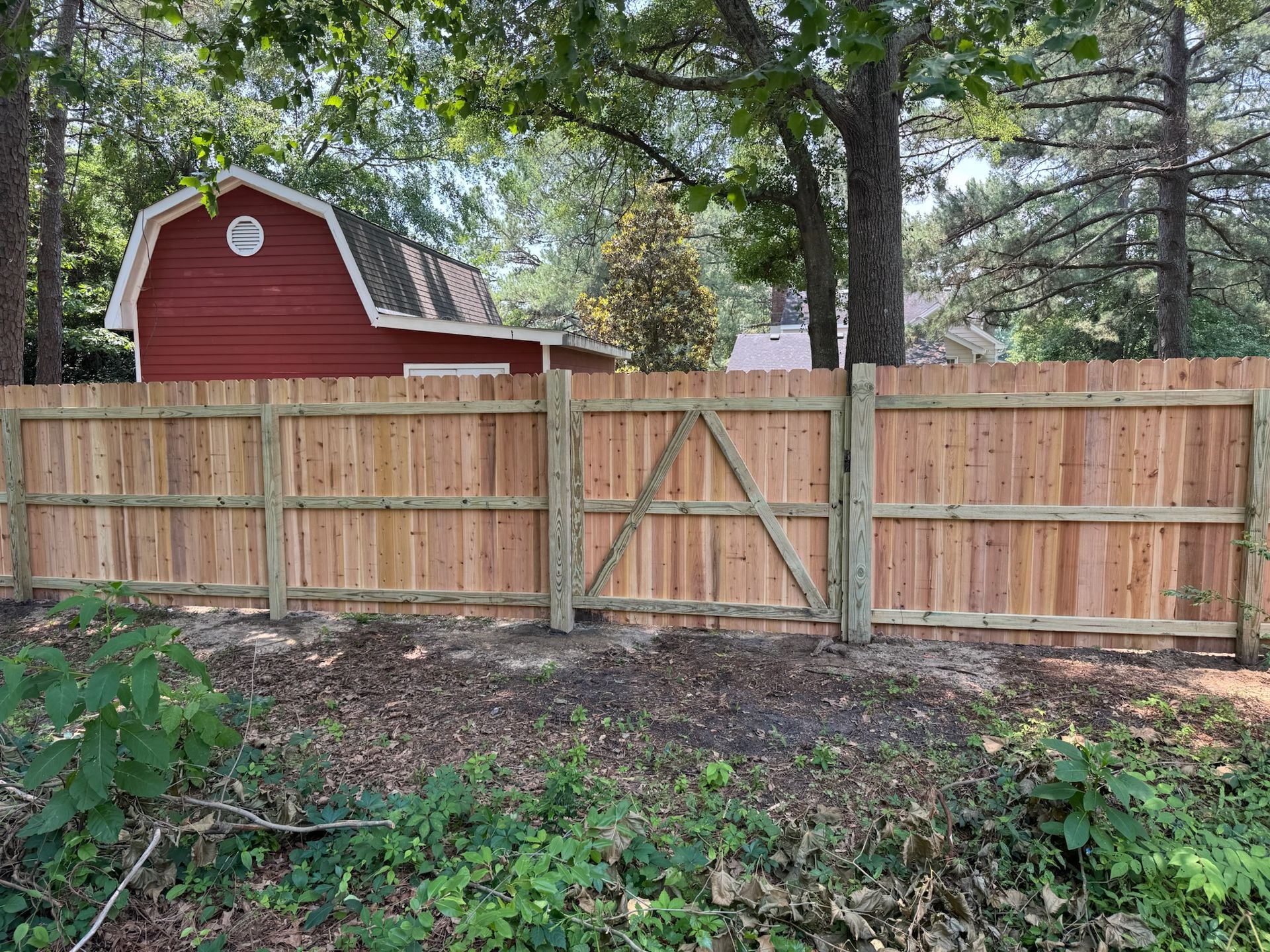A wooden fence with a gate in front of a red barn.