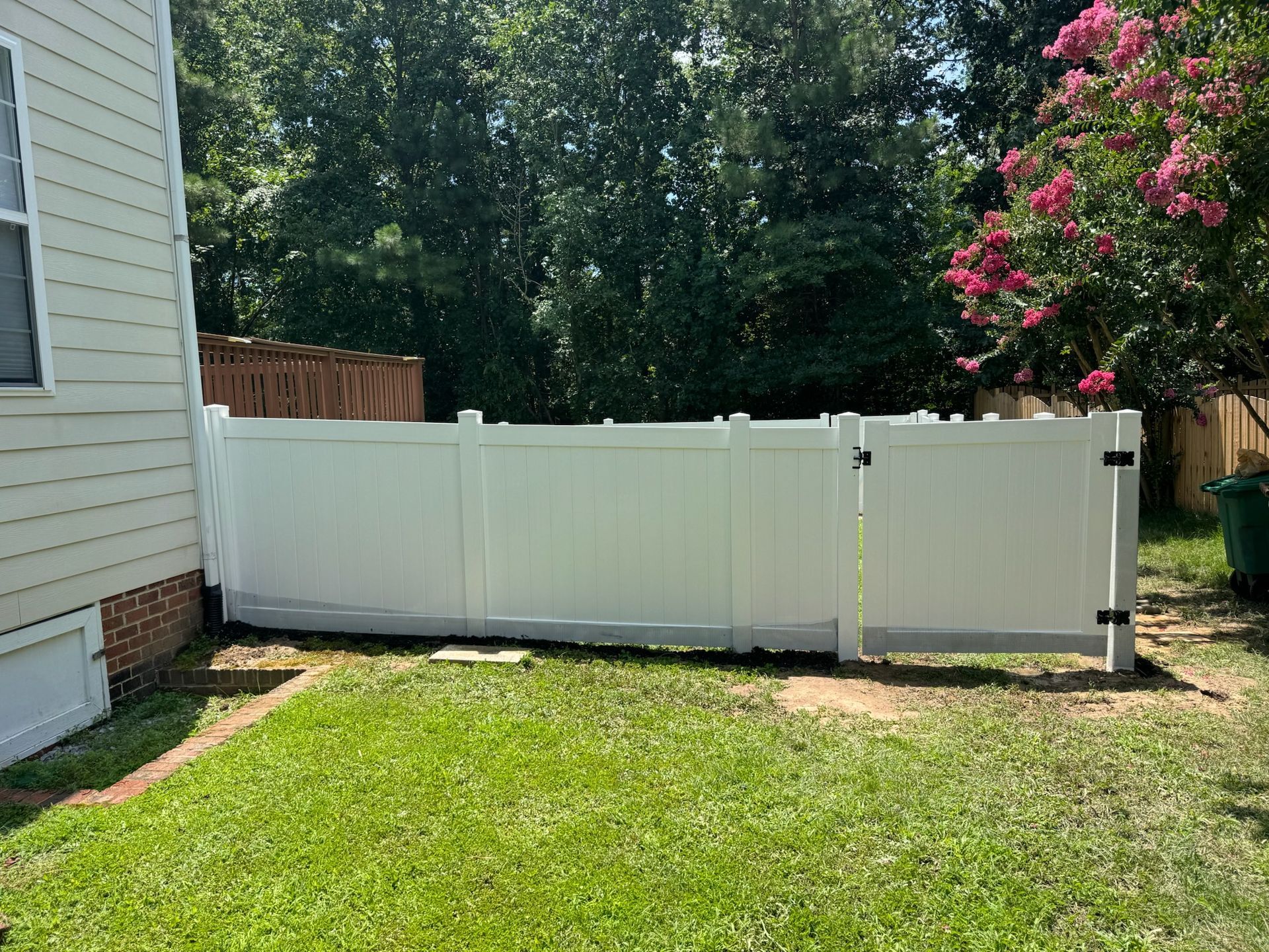 A white fence is in the backyard of a house.