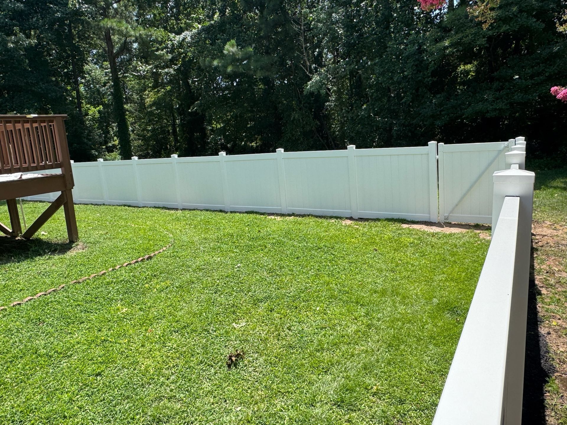 A white fence surrounds a lush green yard with a wooden bench in the background.
