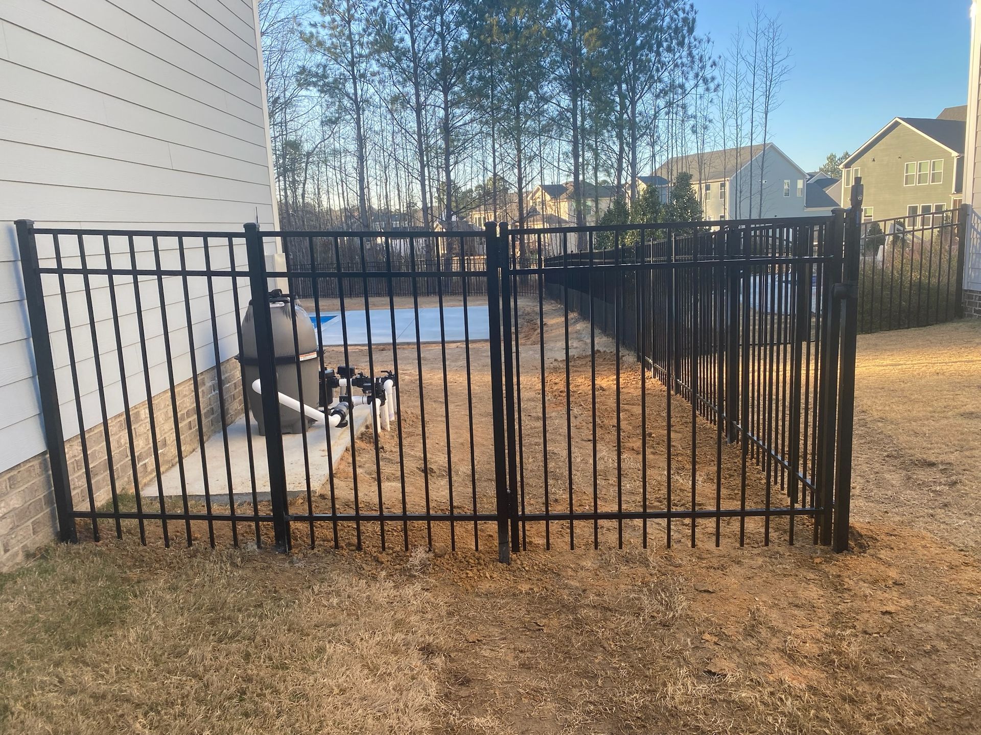 A black metal fence surrounds a yard with a pool in the background.