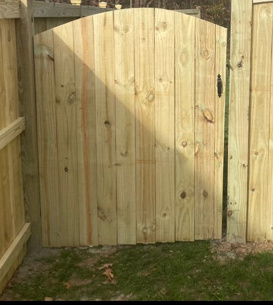 A wooden gate is sitting in the grass next to a wooden fence.