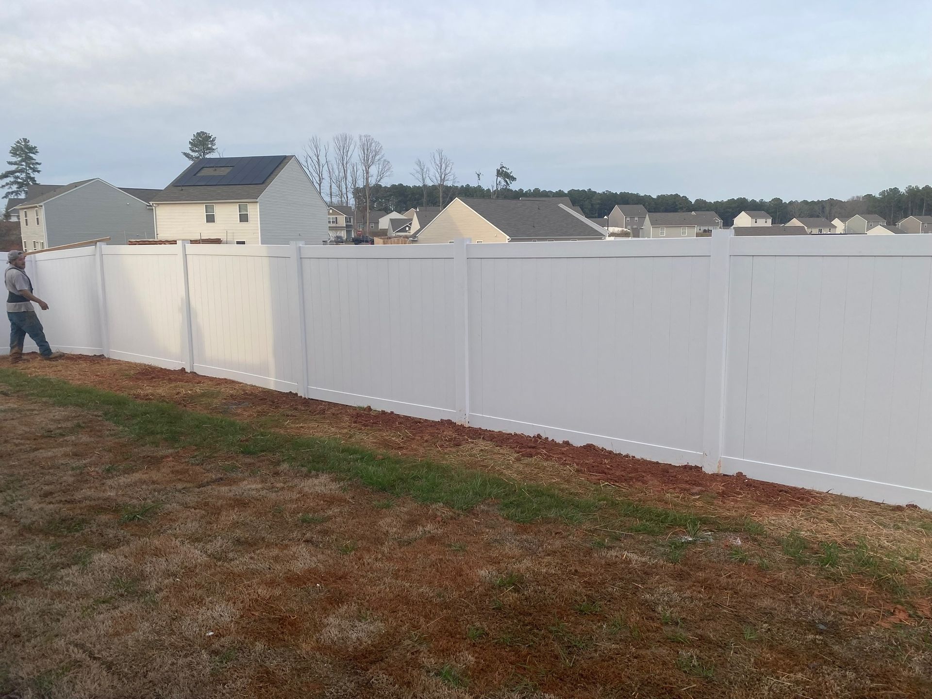 A man is standing next to a white fence in a field.