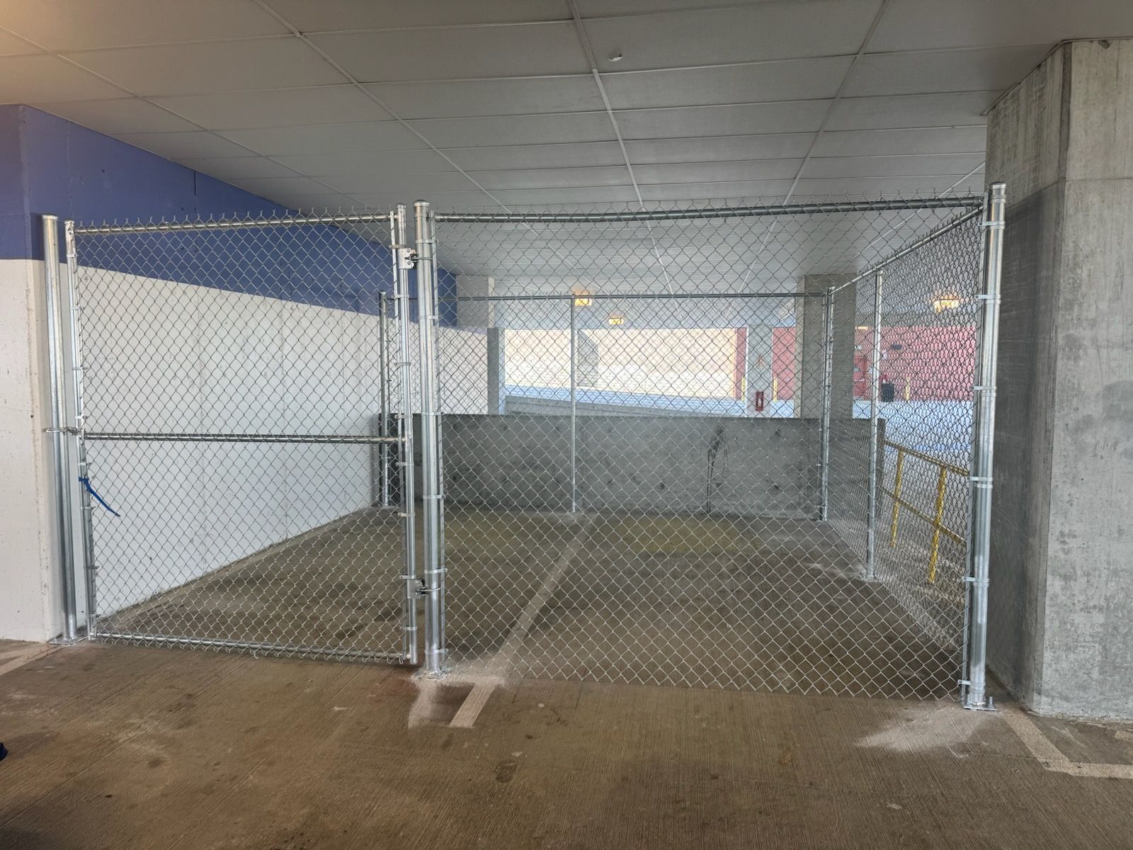 There is a chain link fence in the middle of a parking garage.