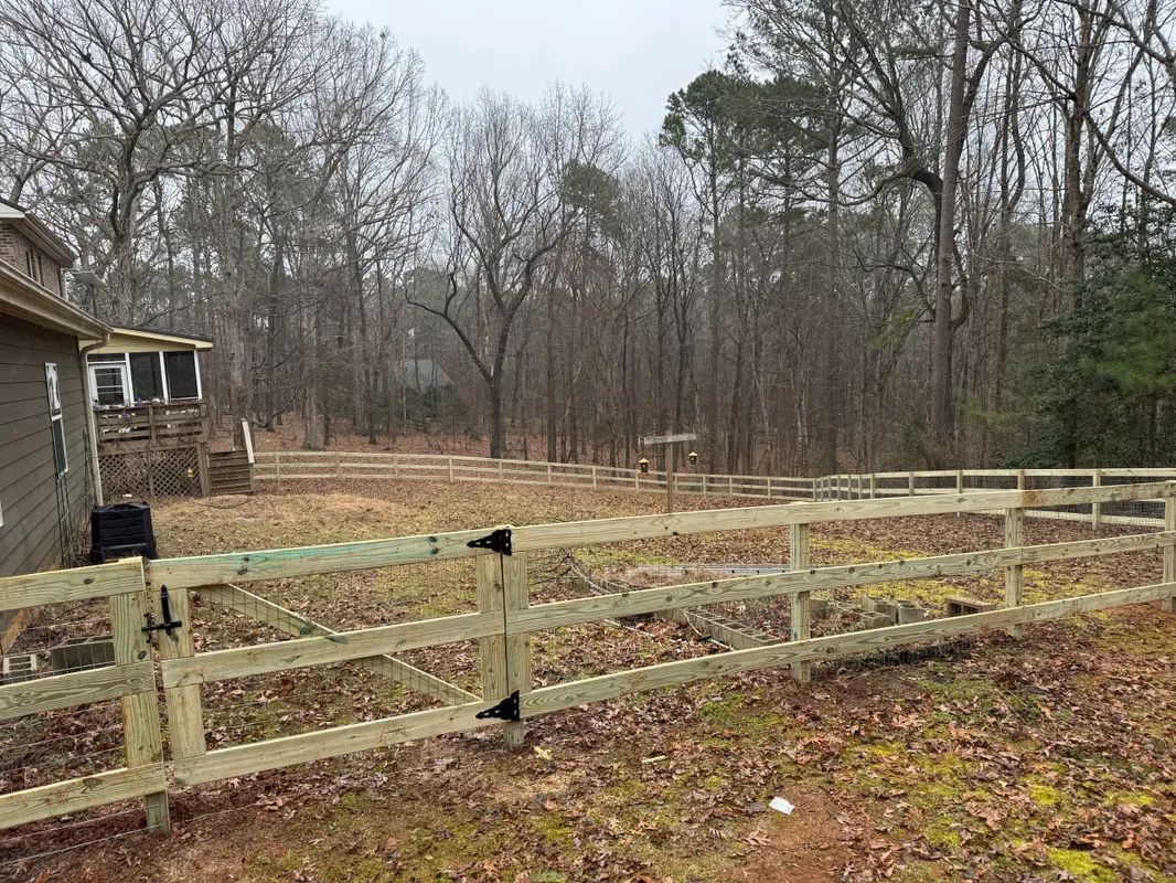 A wooden fence surrounds a house in the woods.