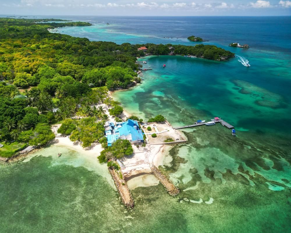 Vista aérea de un complejo turístico en una isla tropical con aguas turquesas, playas de arena blanca y una costa exuberante y verde.