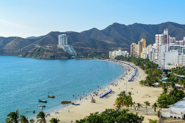 Playa tropical curva con mar azul, montañas y hoteles de gran altura a lo largo de la costa.