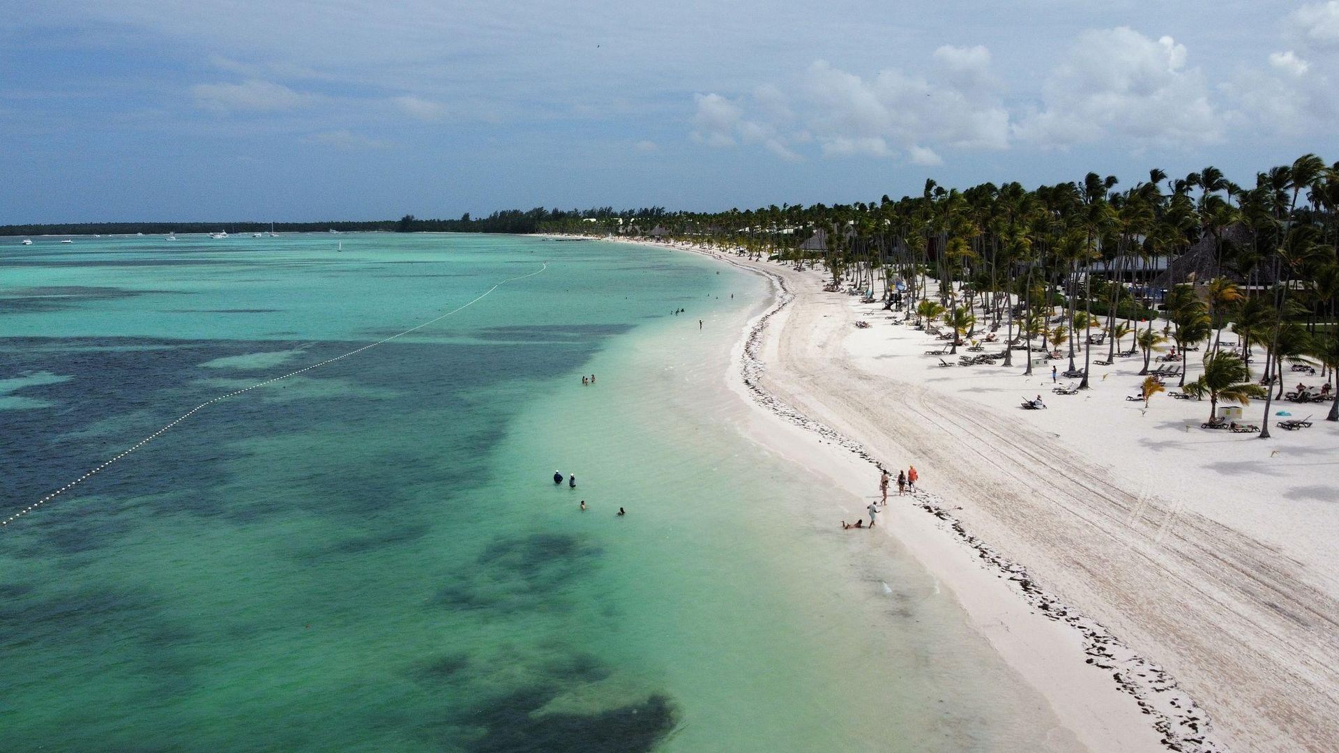 Playa tropical con aguas turquesas, arena blanca y palmeras bajo un cielo nublado.