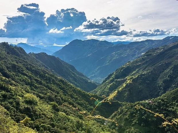 Valle de montaña verde y exuberante bajo un cielo azul brillante con nubes dispersas.